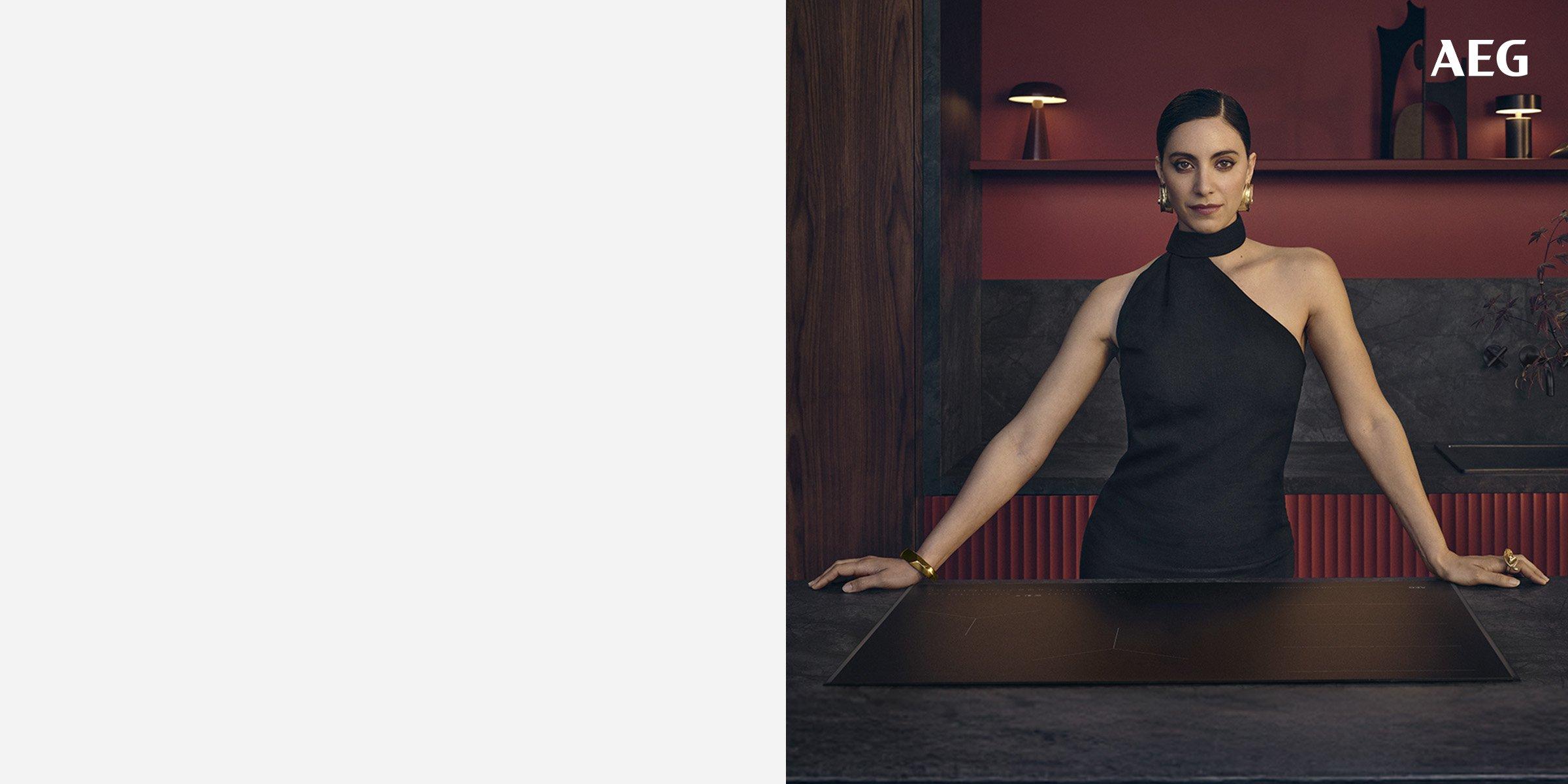 a woman in a elegant kitchen with dark stone countertops, standing confidently behind a sleek AEG induction cooktop.