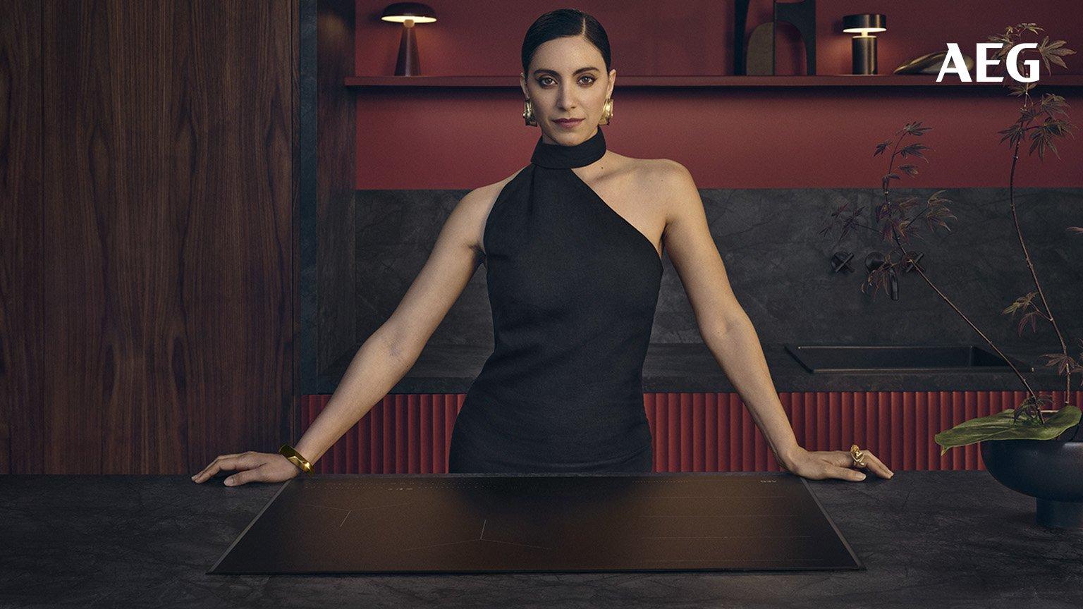 a woman in a elegant kitchen with dark stone countertops, standing confidently behind a sleek AEG induction cooktop.