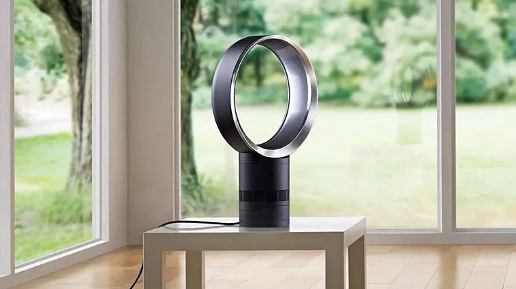 Bladeless tower fan on a small table by large windows, modern home cooling appliance in bright living room.