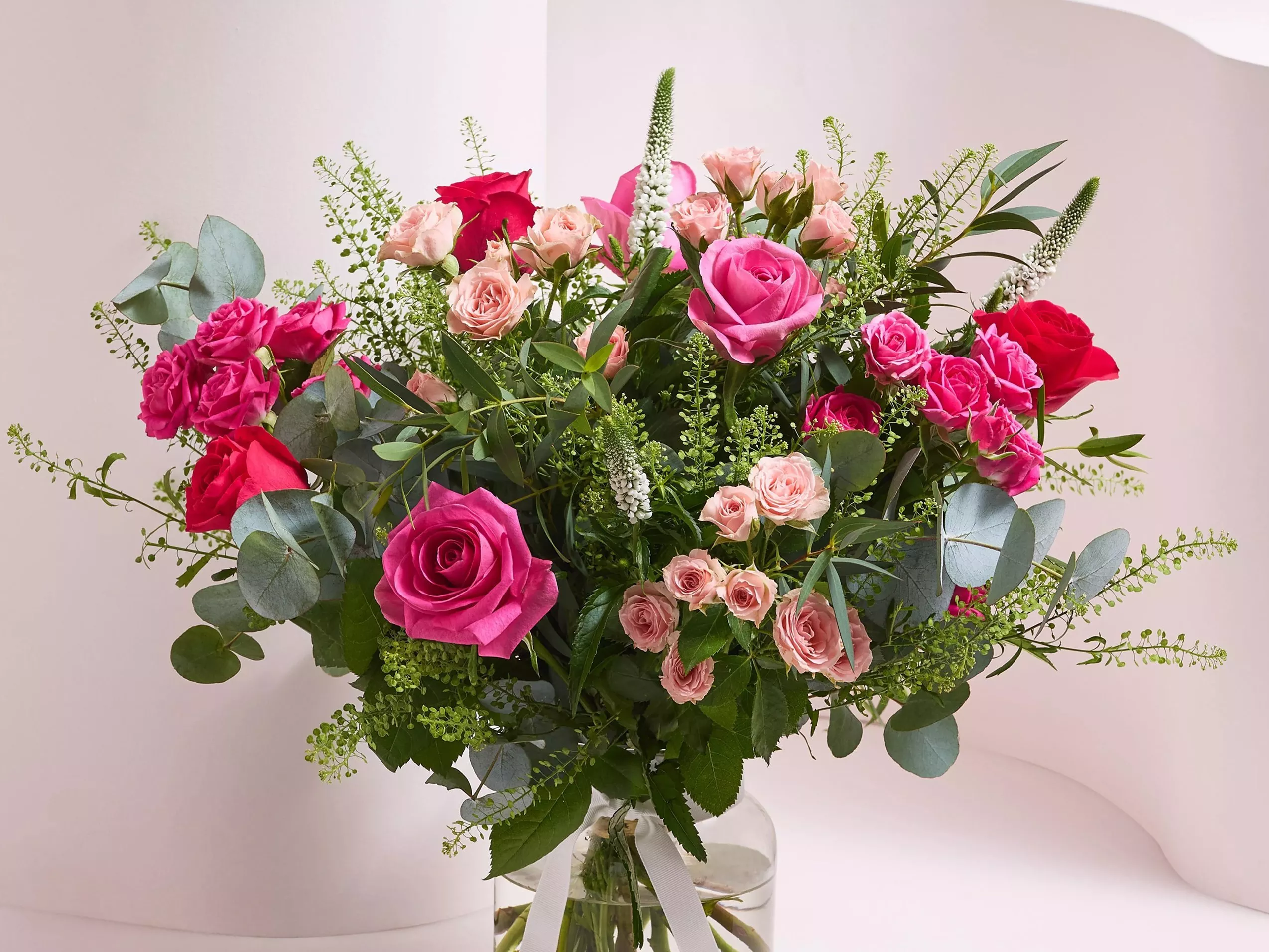 Pink and red rose bouquet with blush spray roses, eucalyptus foliage and white veronica in a glass vase.