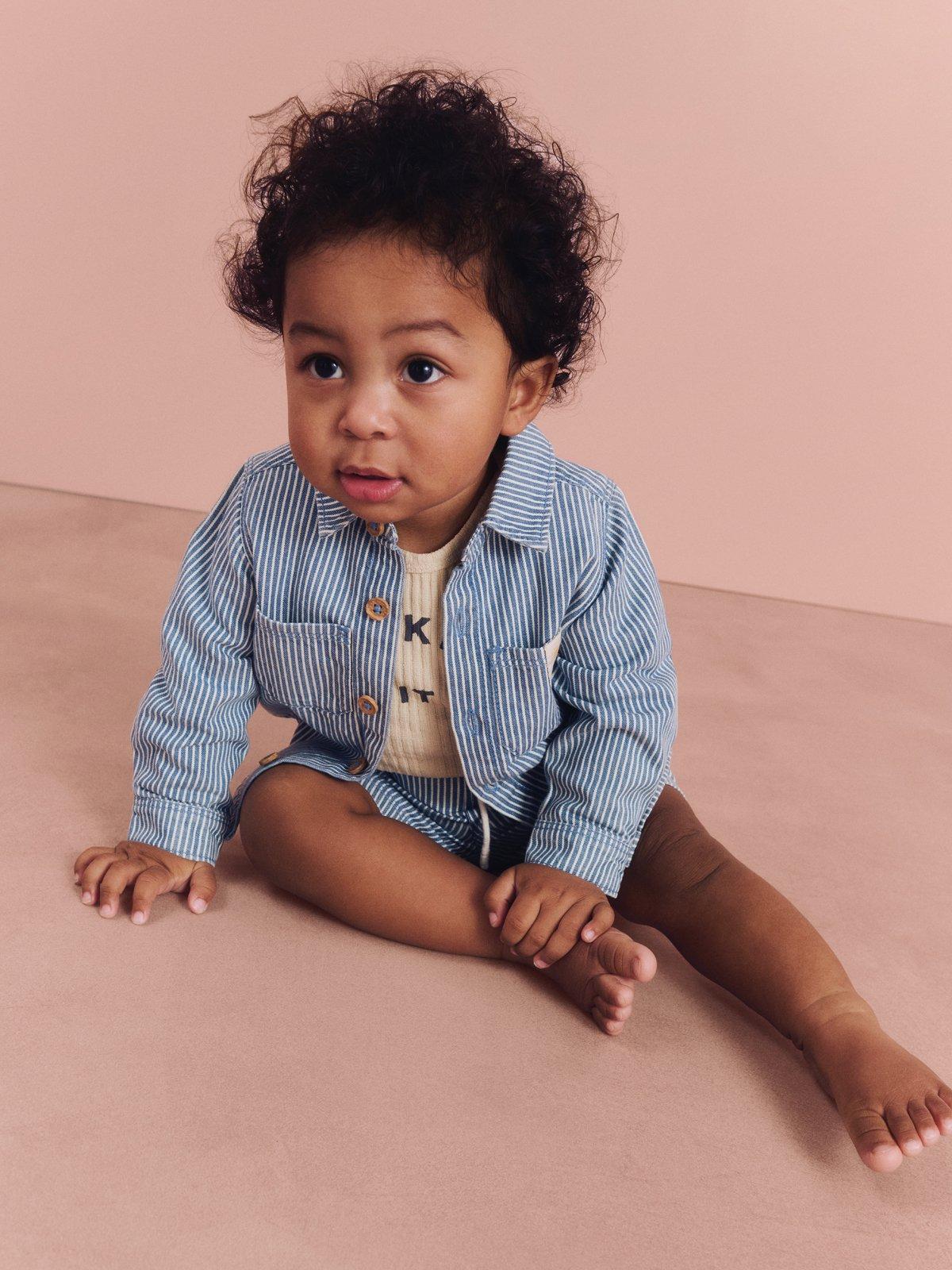 image of a baby wearing a stripy top and bottom sitting on a pink background