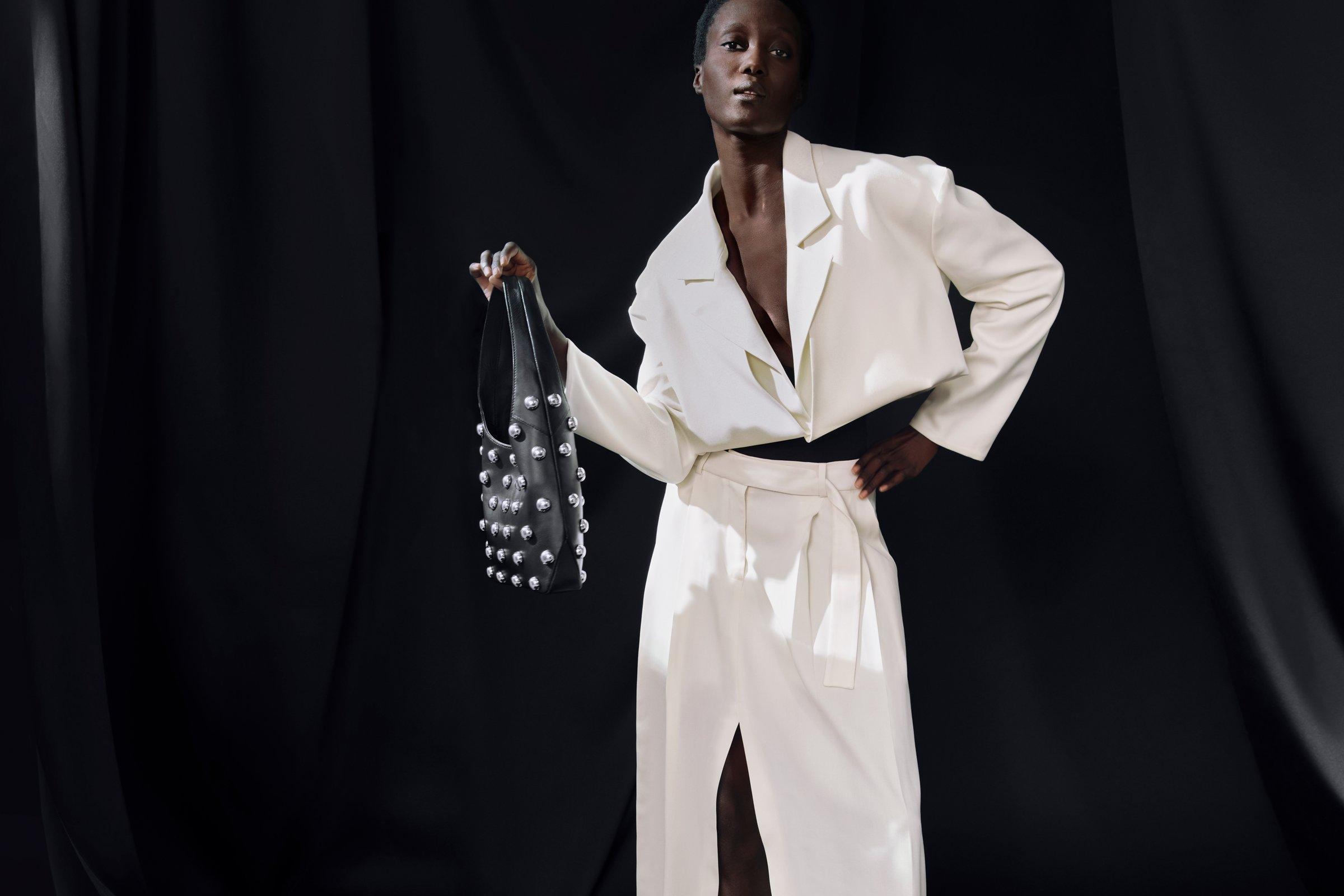 Image of a model wearing a Awake Mode white skirt suit with a black pvc background