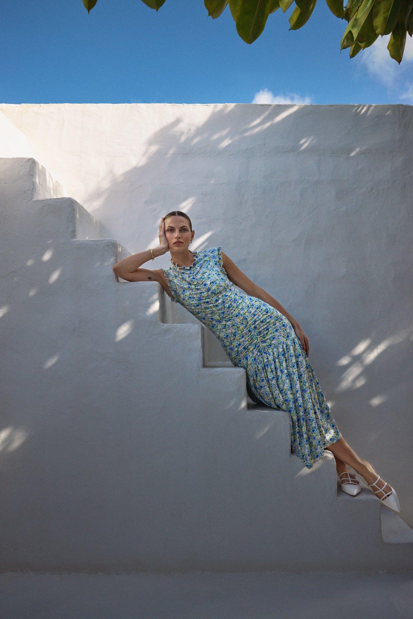 a lady lying on her side on some outdoor stairs wearing a blue floral dress