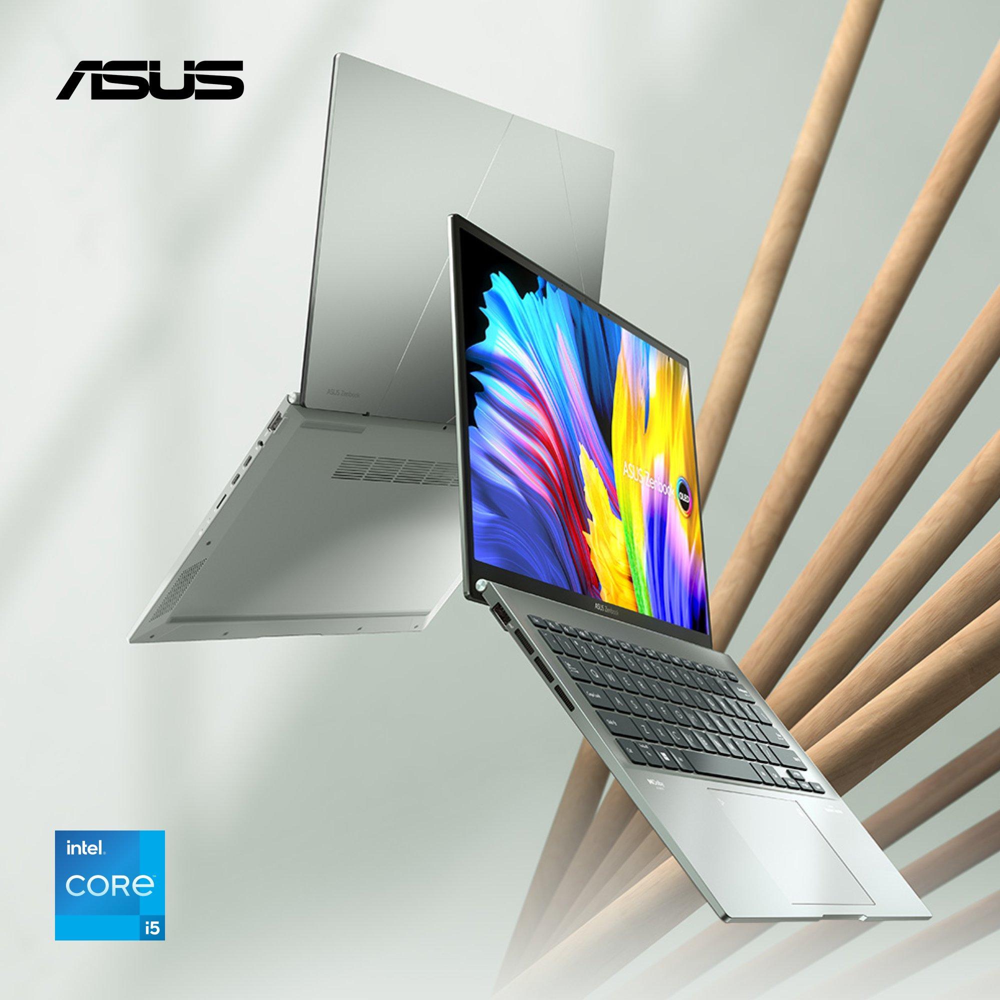 Two slim silver Asus laptops float diagonally in front of a wooden slatted wall. The front laptop is open, showing a colorful abstract image on its screen.