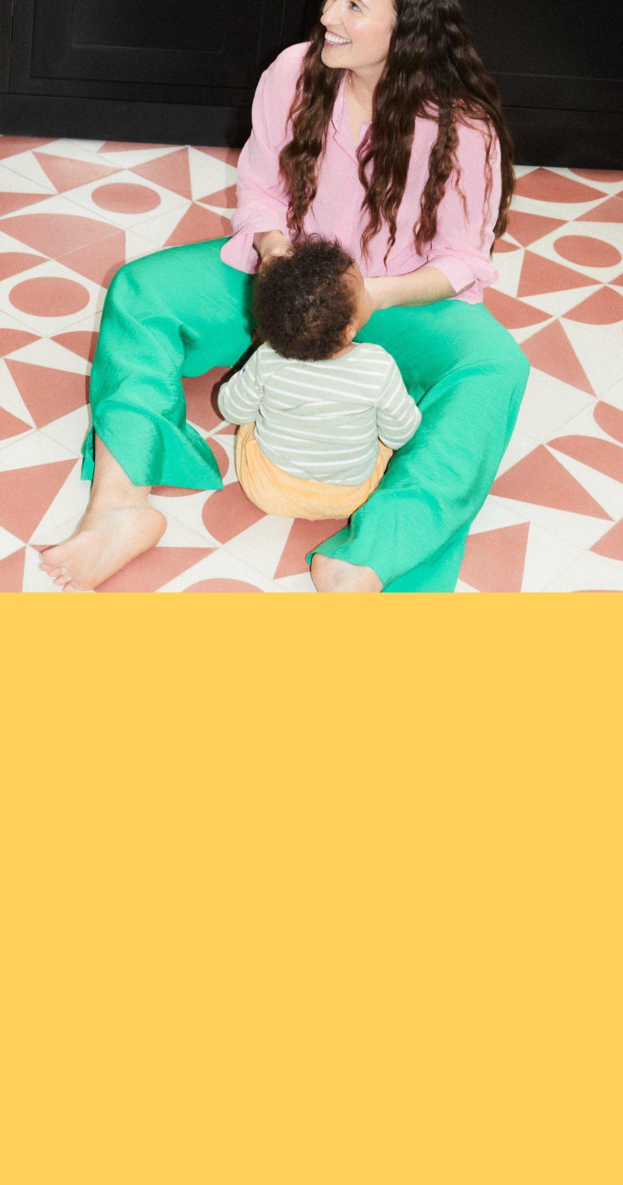 Image of a baby leaning up against it's mother, they are both sitting on the stairs