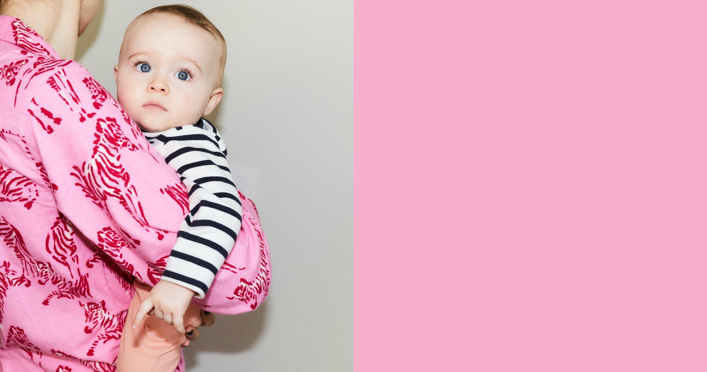 Image of a mother holding a baby wearing a pink top and the baby is looking at the camera