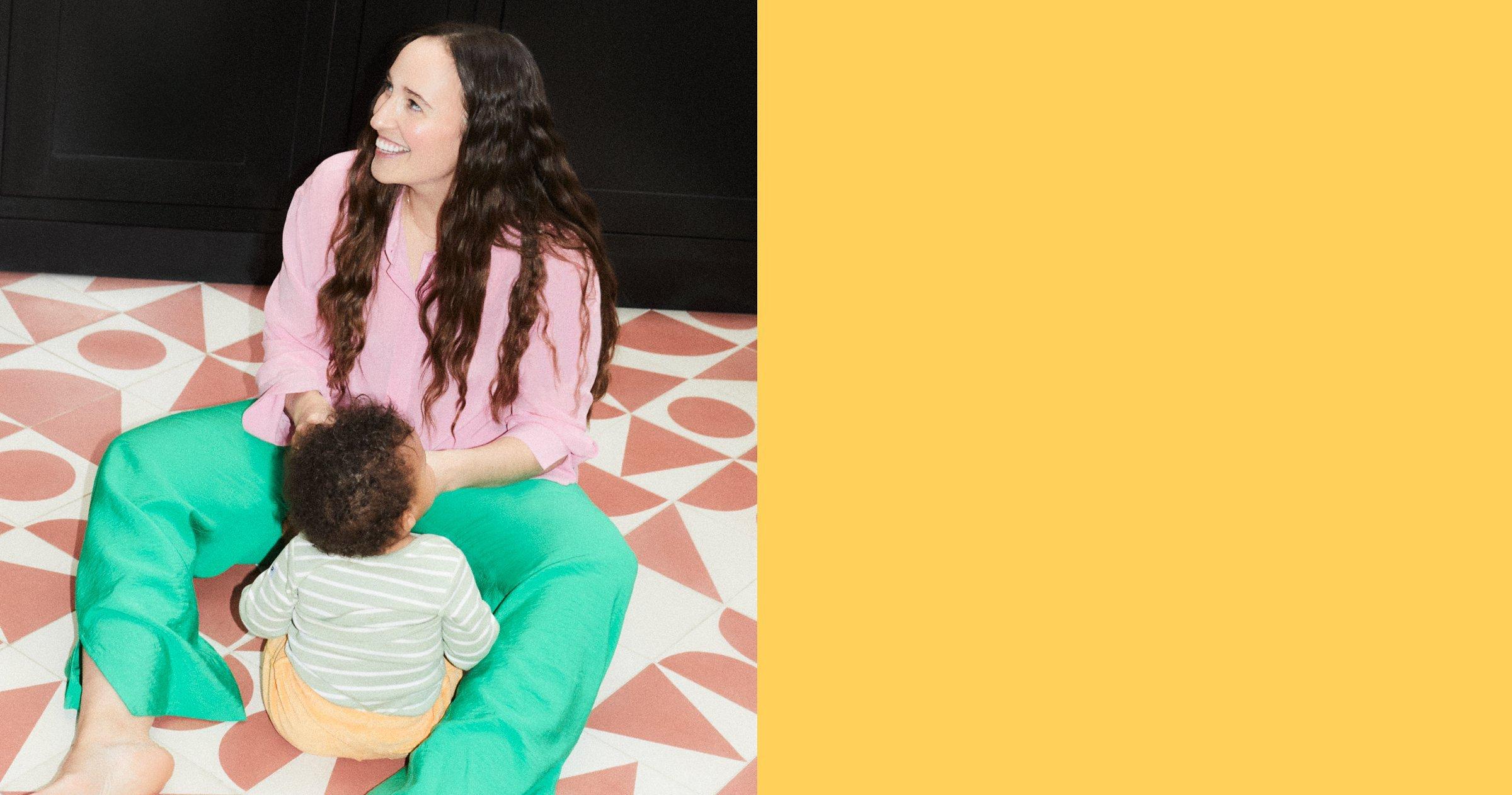 Image of a baby leaning up against it's mother, they are both sitting on the stairs