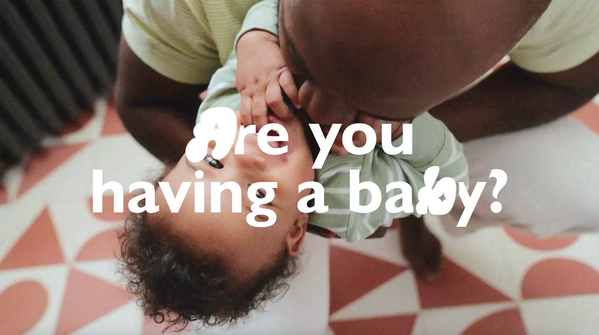 Father lovingly holds a baby upside-down, smiling on a patterned floor. Text reads, "Are you having a baby?"