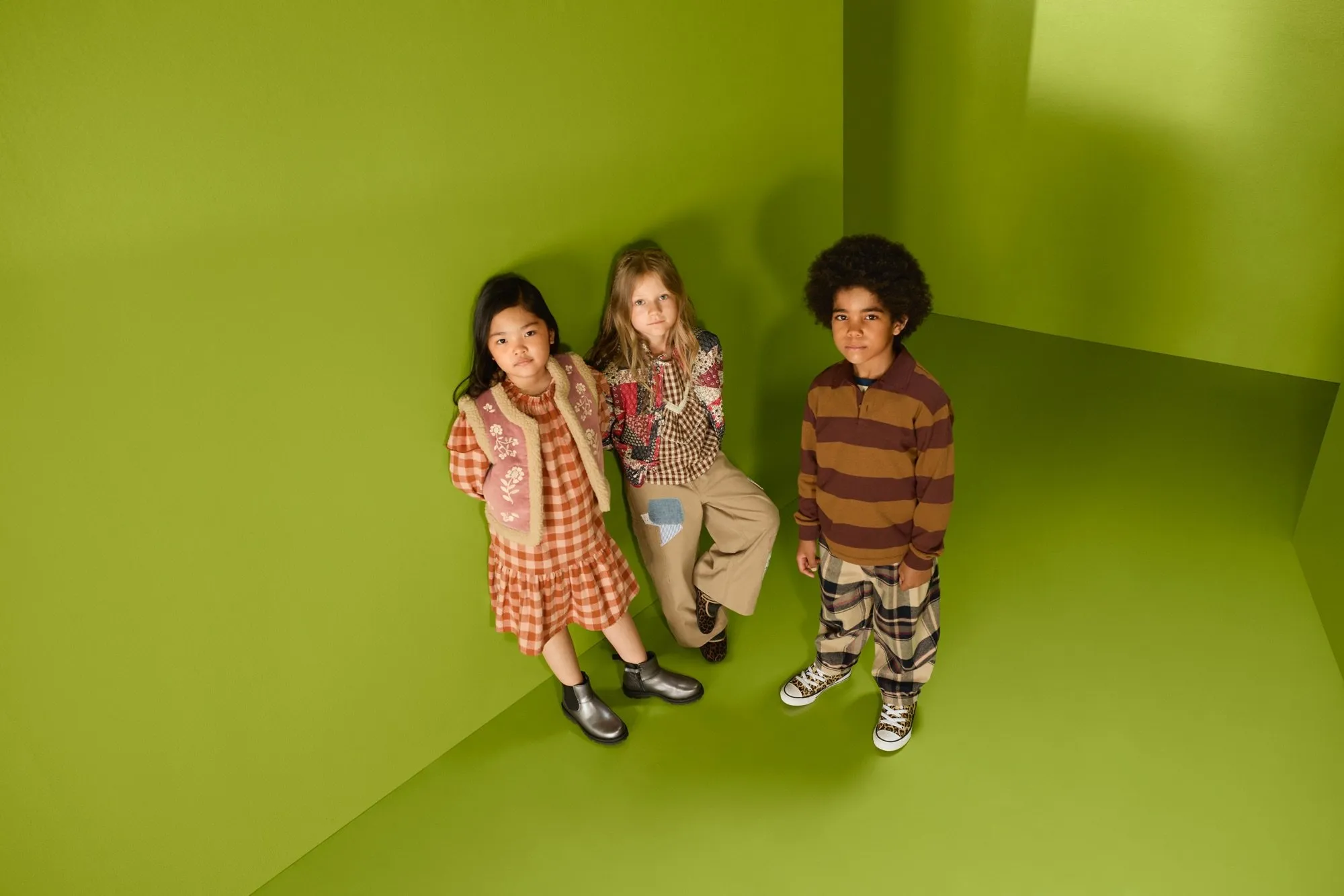 Three children in autumn outfits posing in a green studio corner, showcasing trendy kids fashion styling
