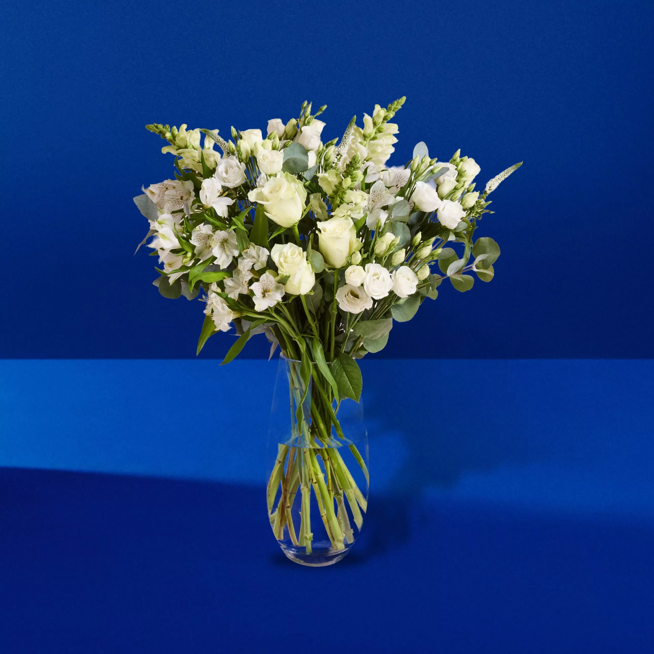 Rose, Lily and Gladioli Hand Tied Bouquet in a glass vase on a blue background