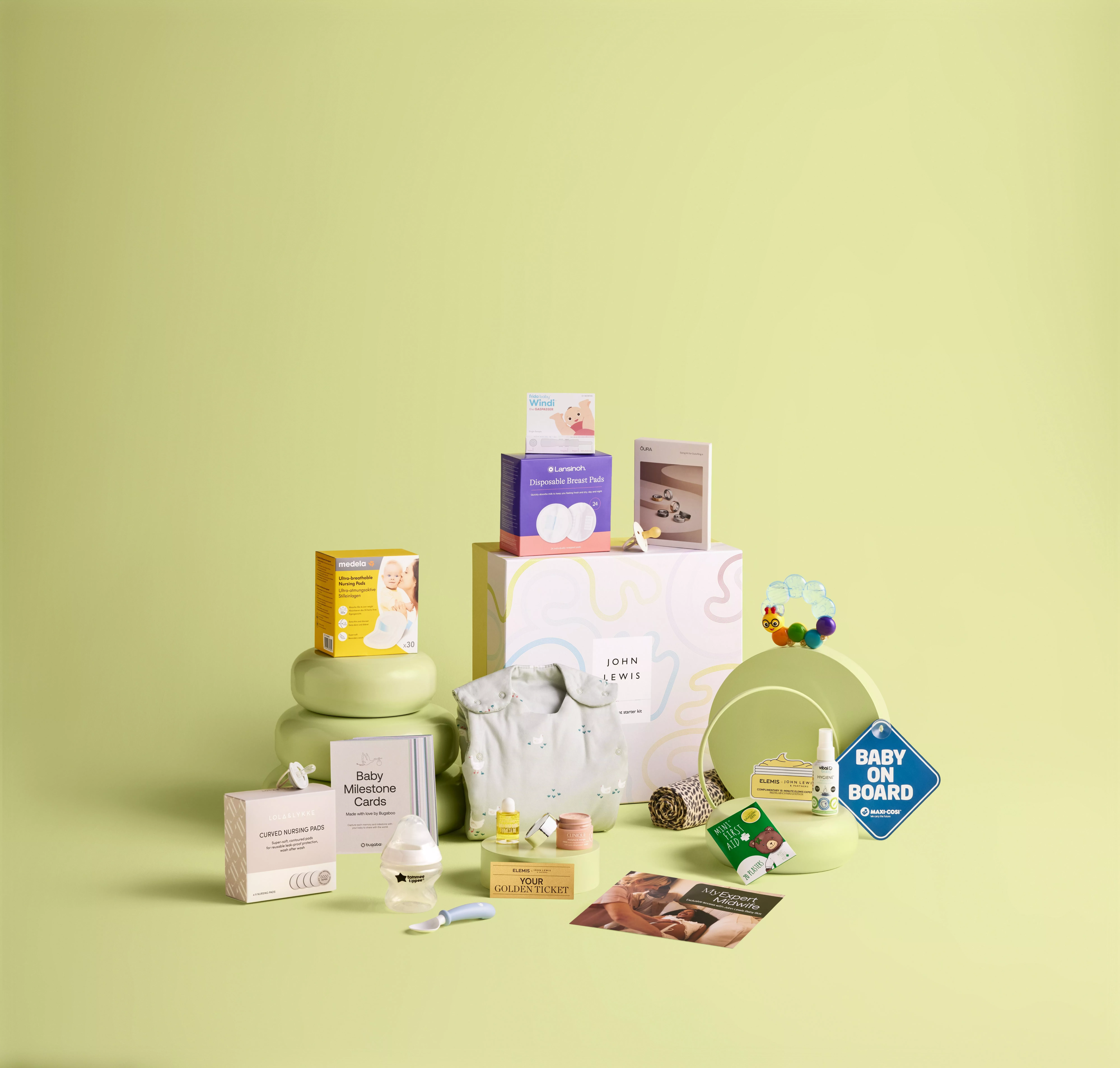 Baby essentials gift set with clothing, skincare, nursing pads, and milestone cards on a light green backdrop.