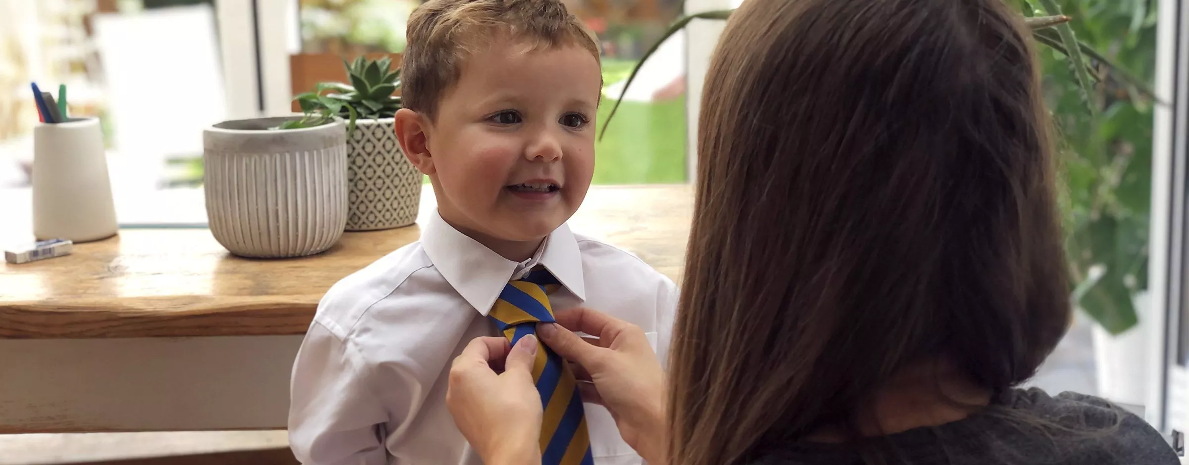 Mother adjusts young boy’s school tie and shirt at home, preparing for first day of primary school morning routine