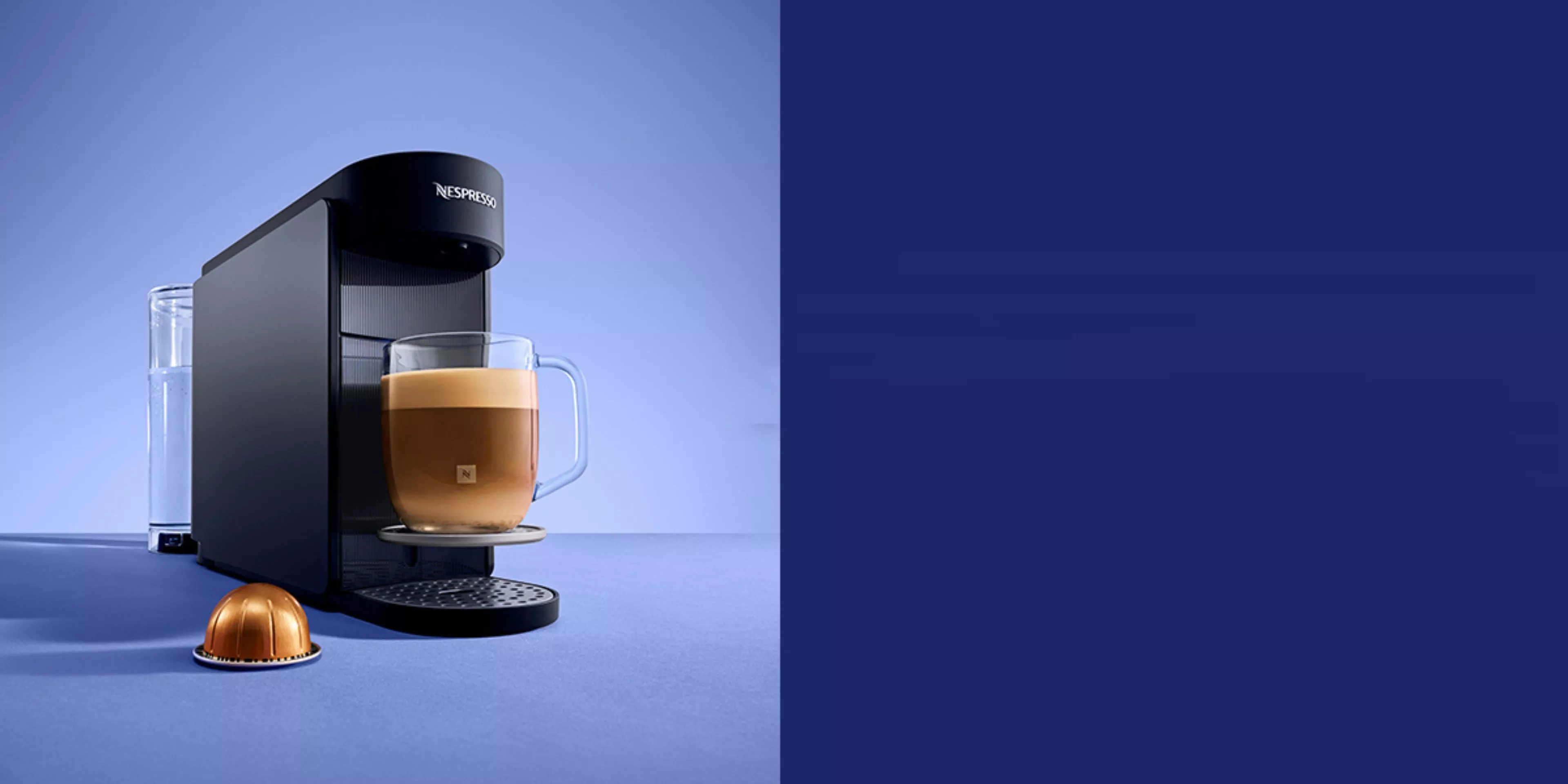 Nespresso pod coffee machine brewing a latte in glass mug, with water tank and capsule on blue background