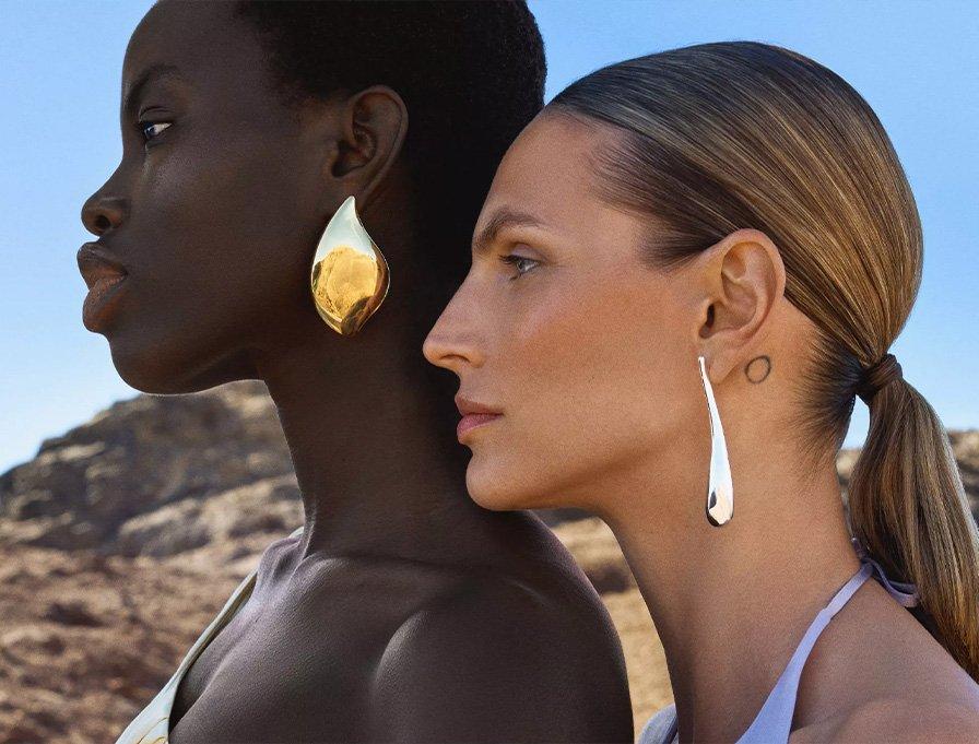 A women wearing gold earungs, standing in front of a woman wearing silver earings