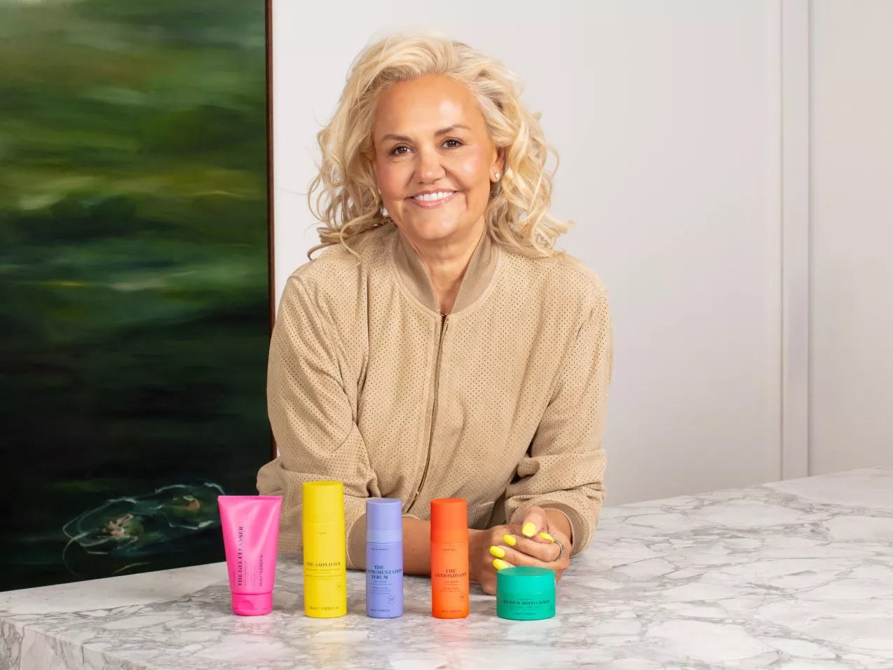 Smiling woman at marble counter with colourful skincare products, beauty brand packaging and indoor studio backdrop