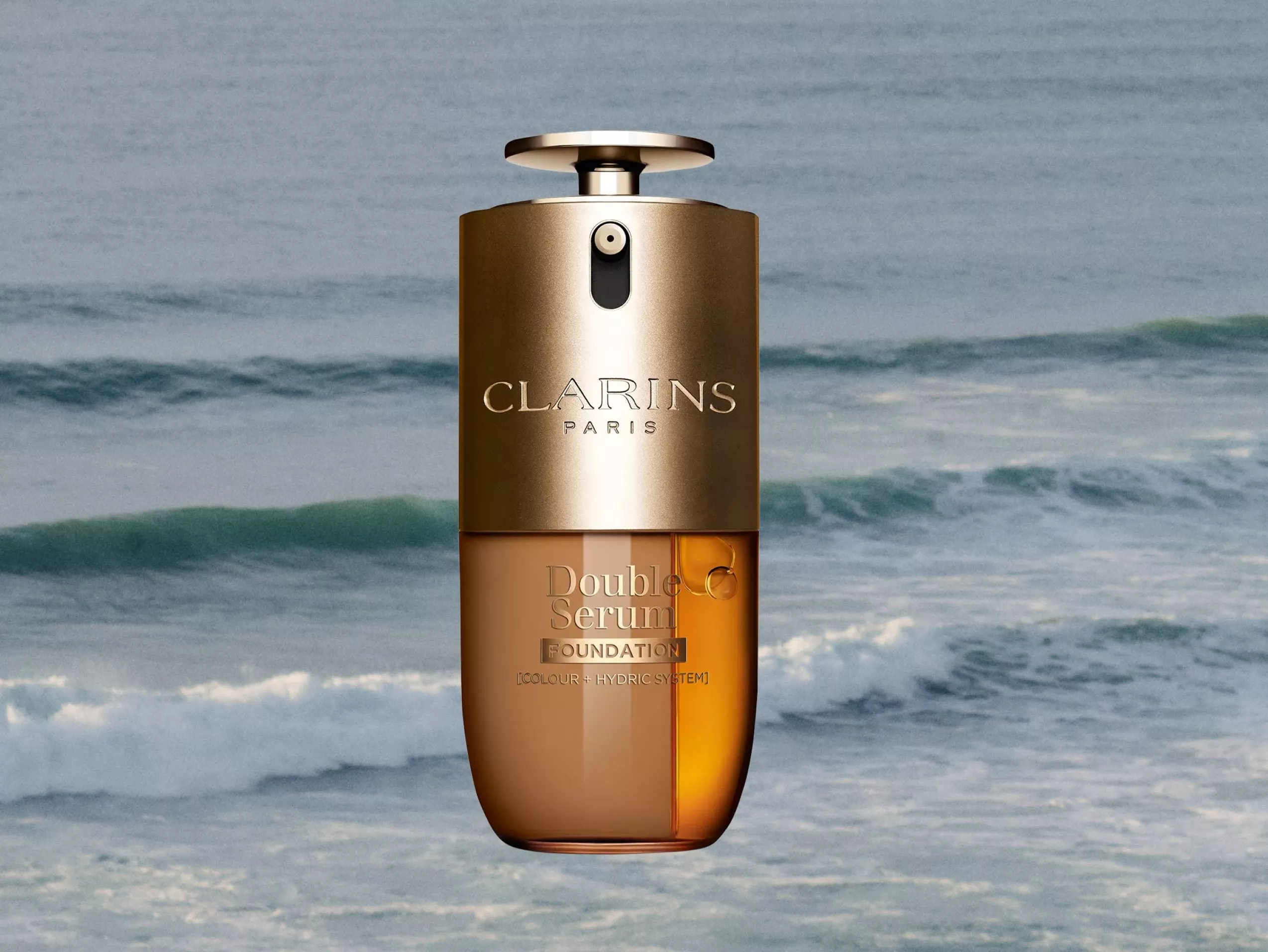 Clarins Double Serum Foundation bottle with a golden cap, set against a serene ocean wave background.