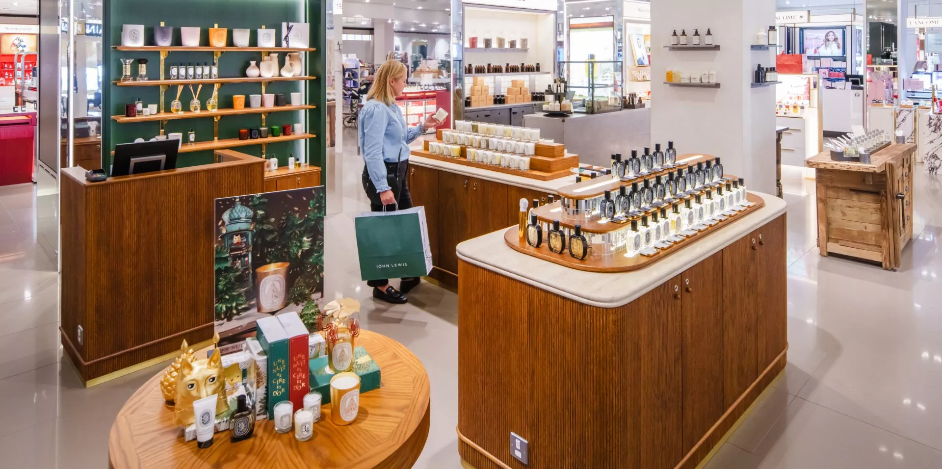 A woman shops in a luxury department store, surrounded by elegantly displayed perfumes and candles.