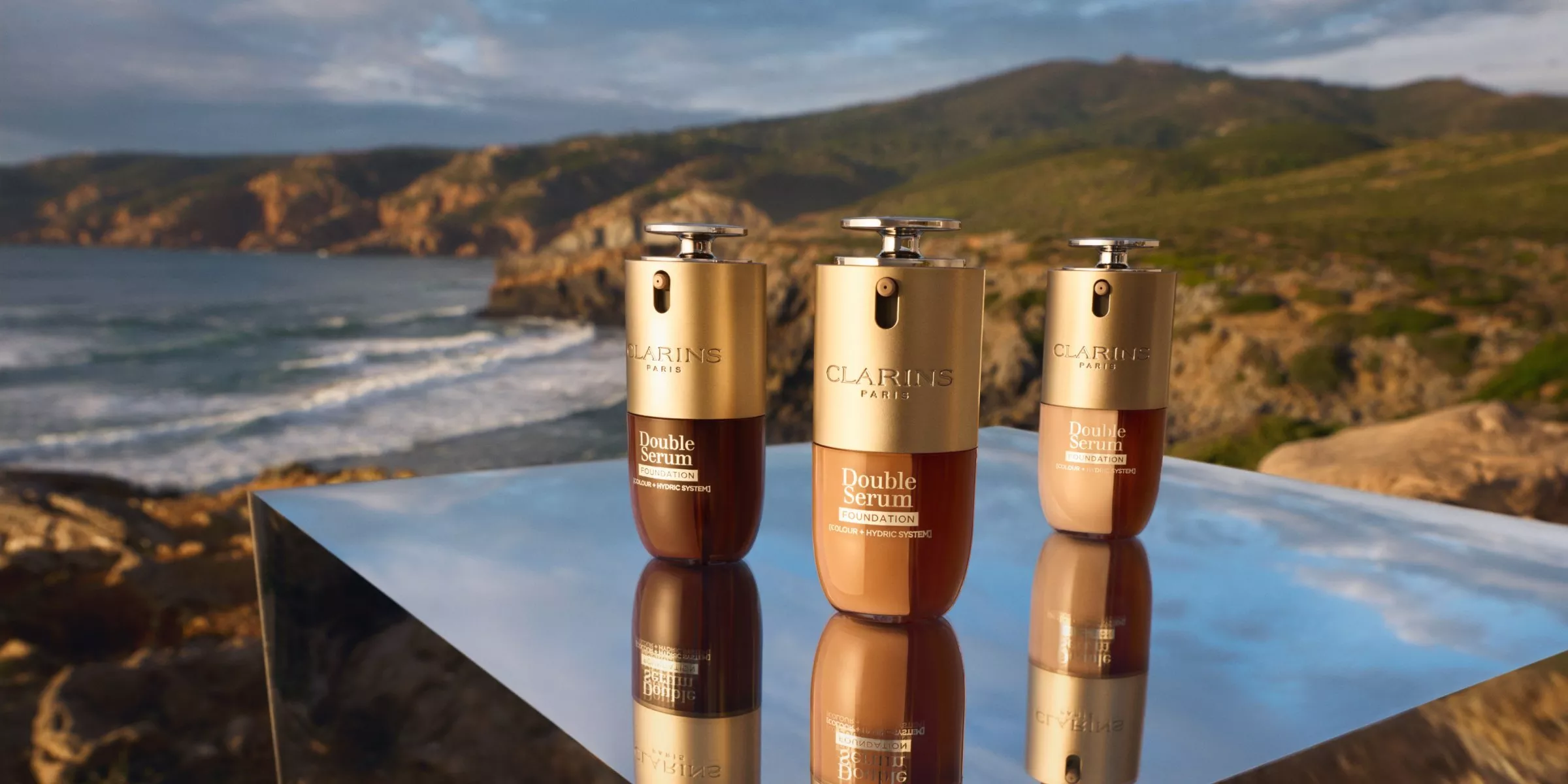 Stylish duo in denim outfits pose outdoors; one in a fitted jacket, the other in a loose shirt. Trees in the background.