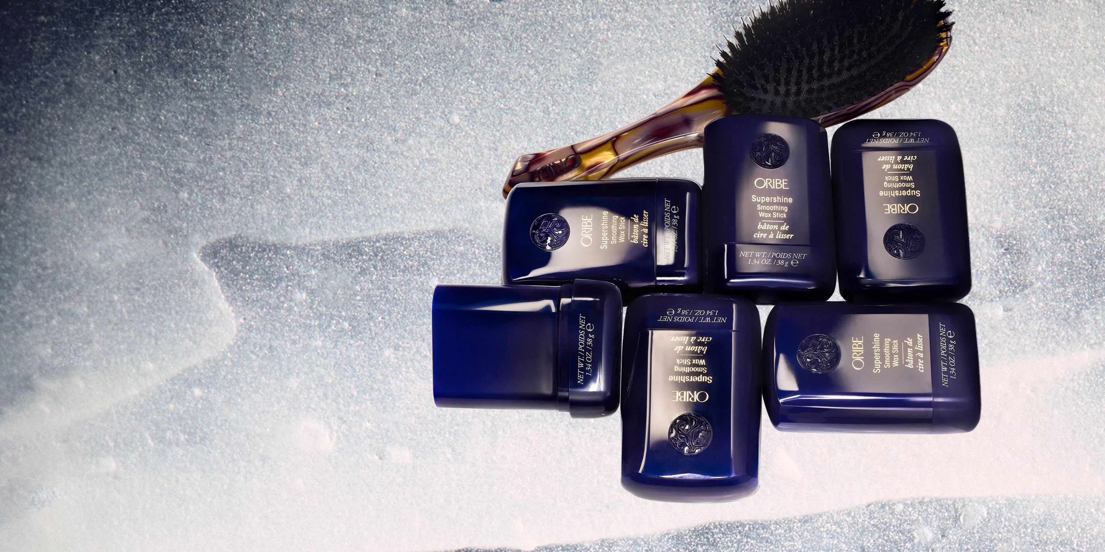 Oribe Supershine hair styling products and boar bristle brush on glittery background, flat lay beauty shot