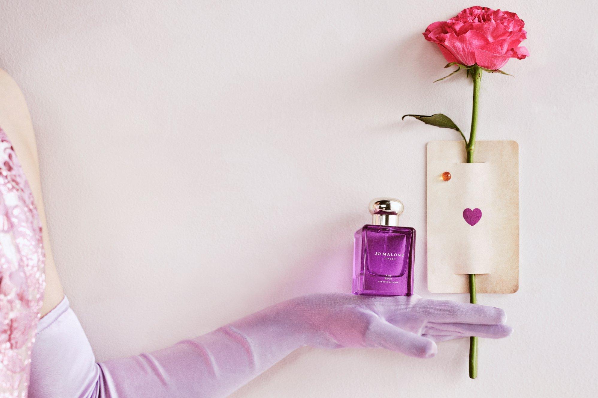 Image of a lady wearing a light purple glove, holding a pink rose and balancing the new Jo Malone fragrance in a purple bottle