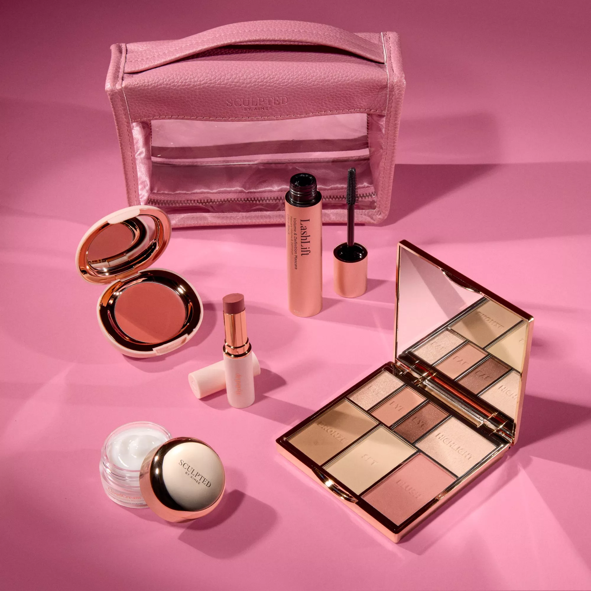 Pink makeup bag with mascara, lipstick, bronzer, face cream and eyeshadow palette on a pink background.