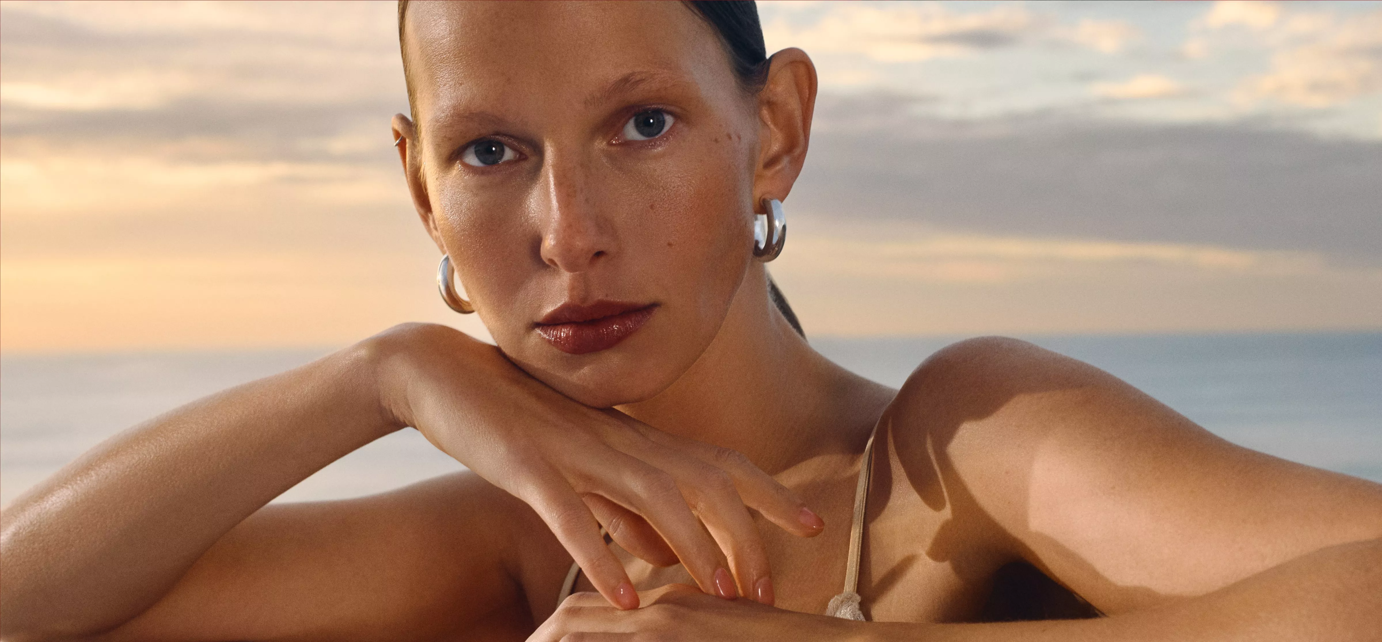 A serene sunset background with a person wearing eyecream and makeup