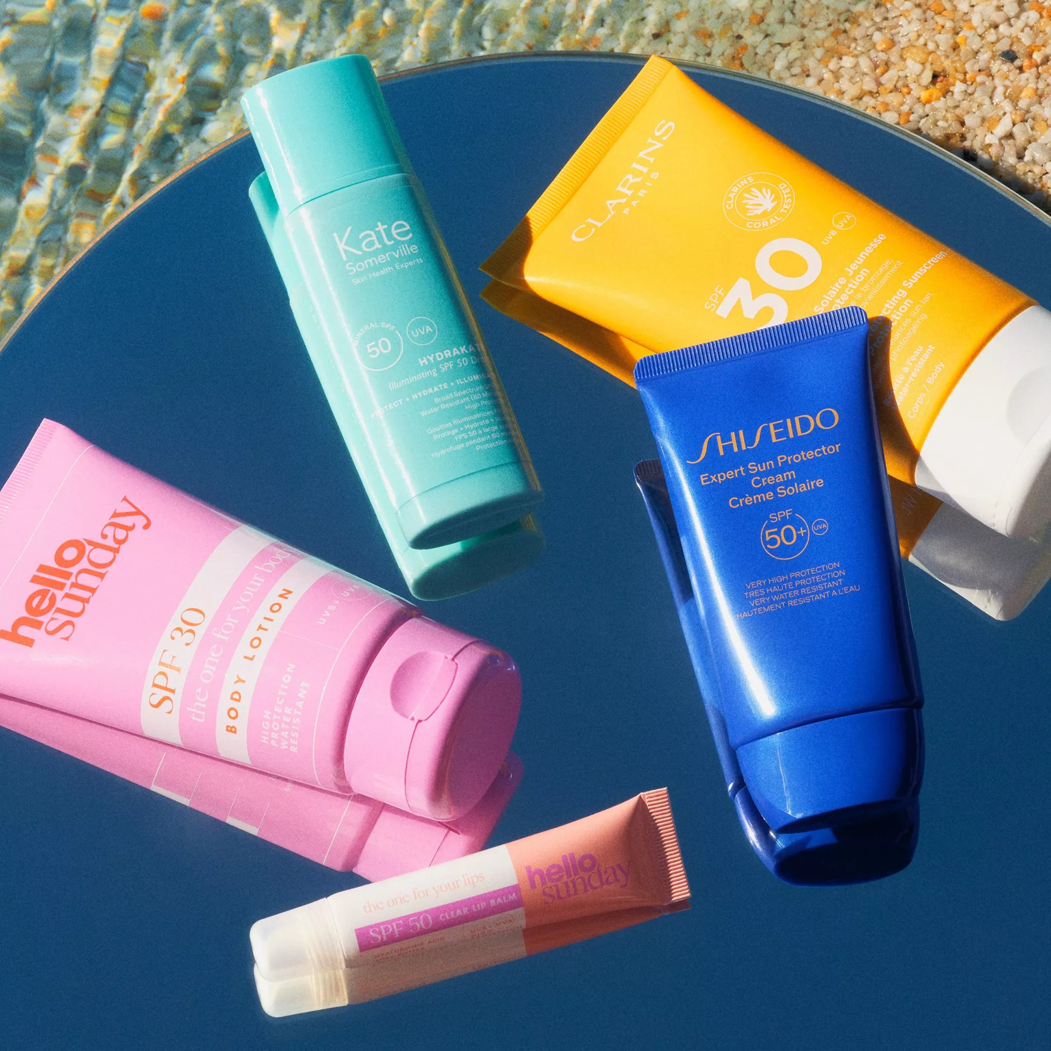 Assorted sunscreen products displayed on a reflective surface, set against a water backdrop.
