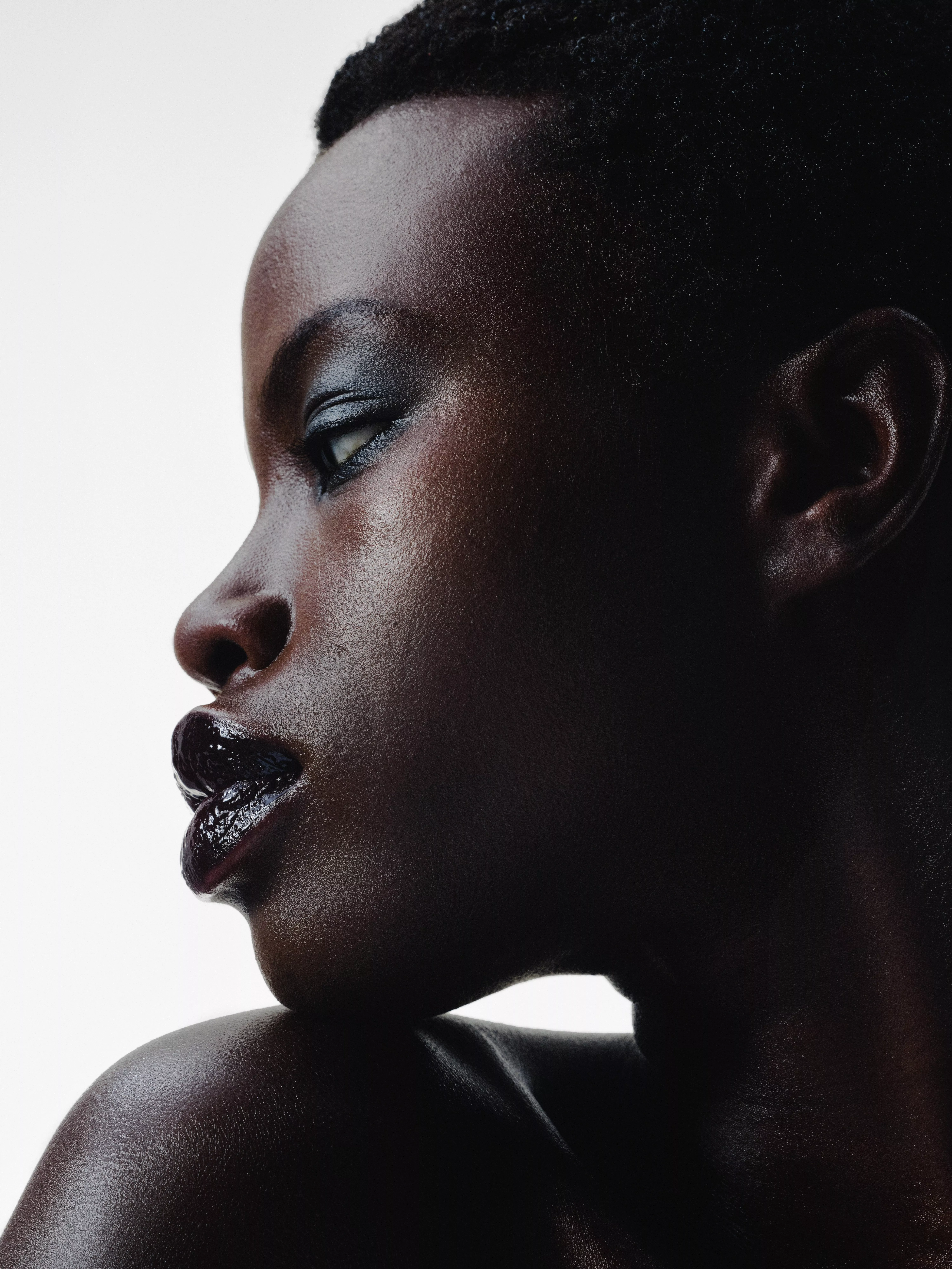 Close-up side profile portrait of a Black woman with glossy lips and smoky eye make-up on a white background