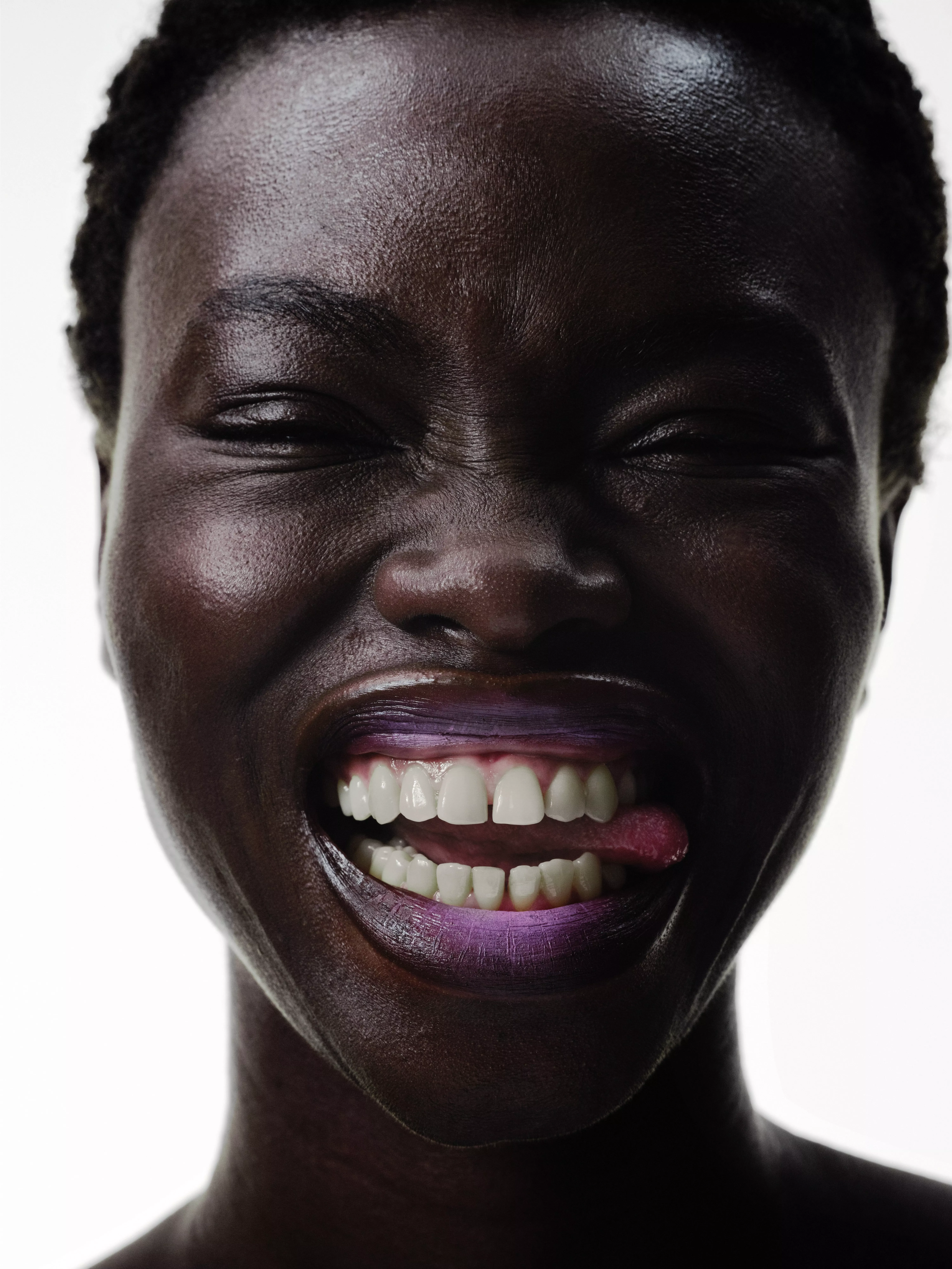 Close-up portrait of a laughing woman with purple lipstick, bright white teeth and joyful expression on white background