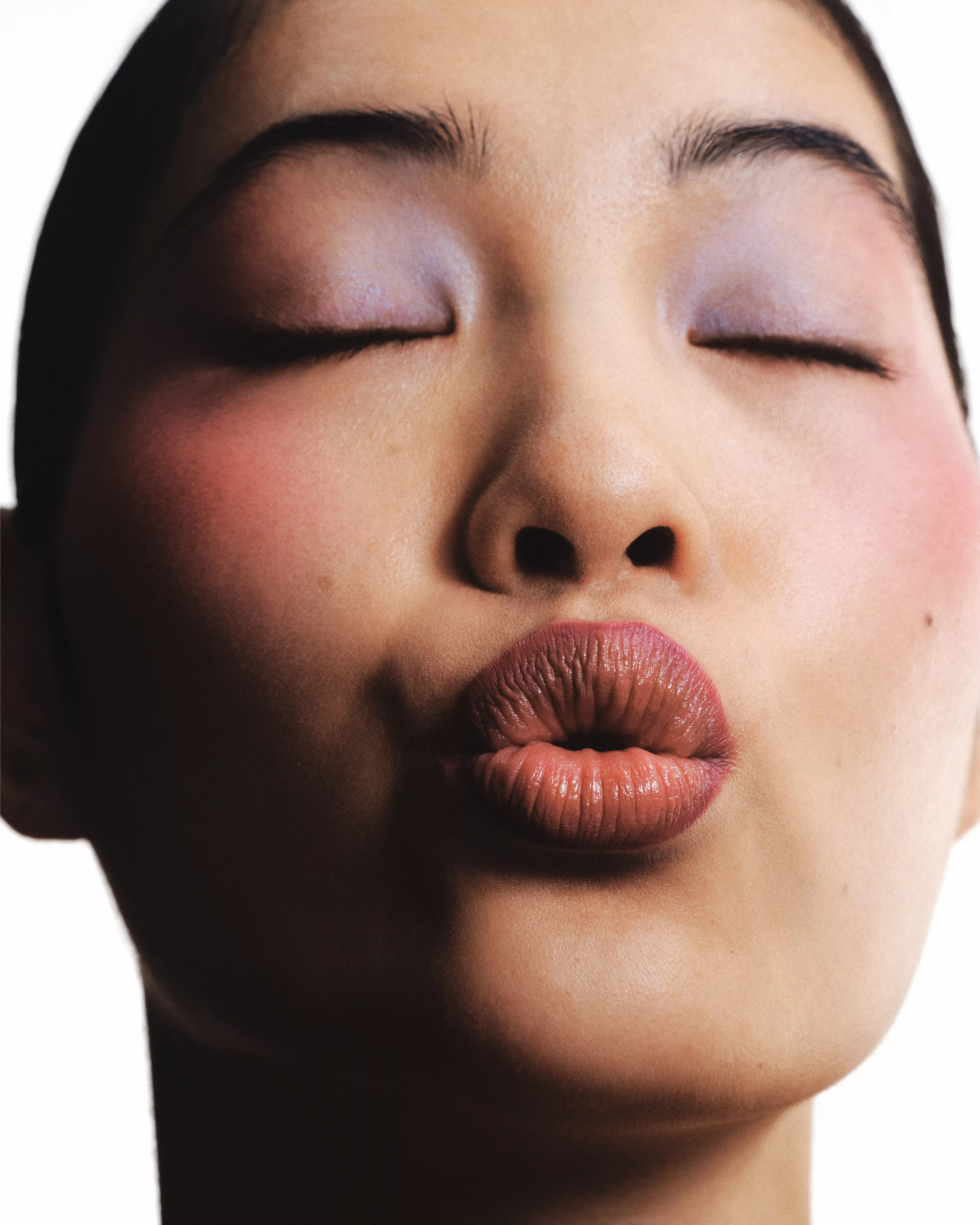 Close-up beauty portrait of a woman with eyes closed, puckered lips, and natural make-up on white background