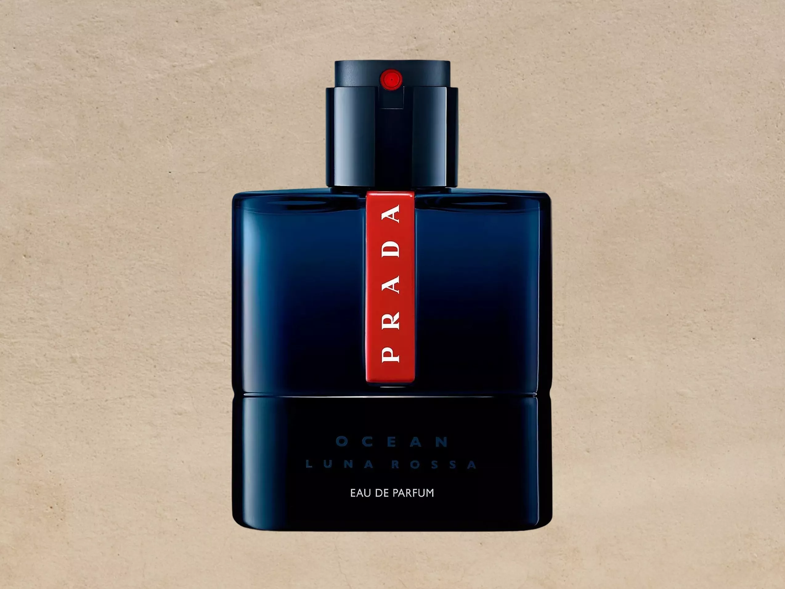 Prada Luna Rossa Ocean Eau de Parfum bottle in dark blue with red logo strip on beige stone background
