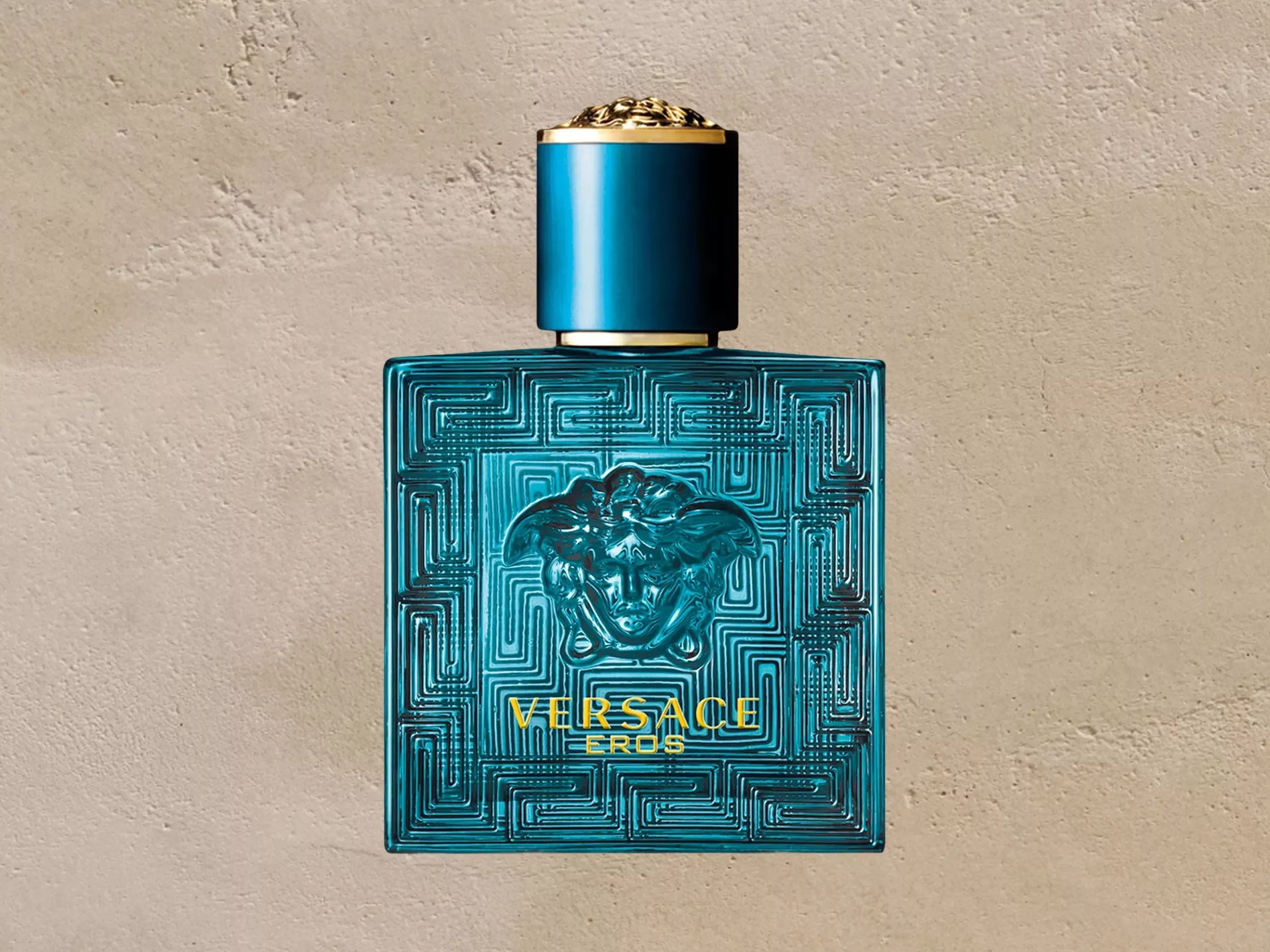Versace Eros turquoise blue men's perfume bottle with Medusa logo and Greek key pattern on stone background