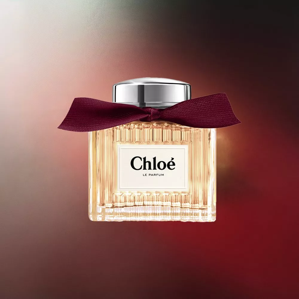 Chloé Le Parfum fragrance bottle with burgundy ribbon bow and silver cap on warm red gradient background