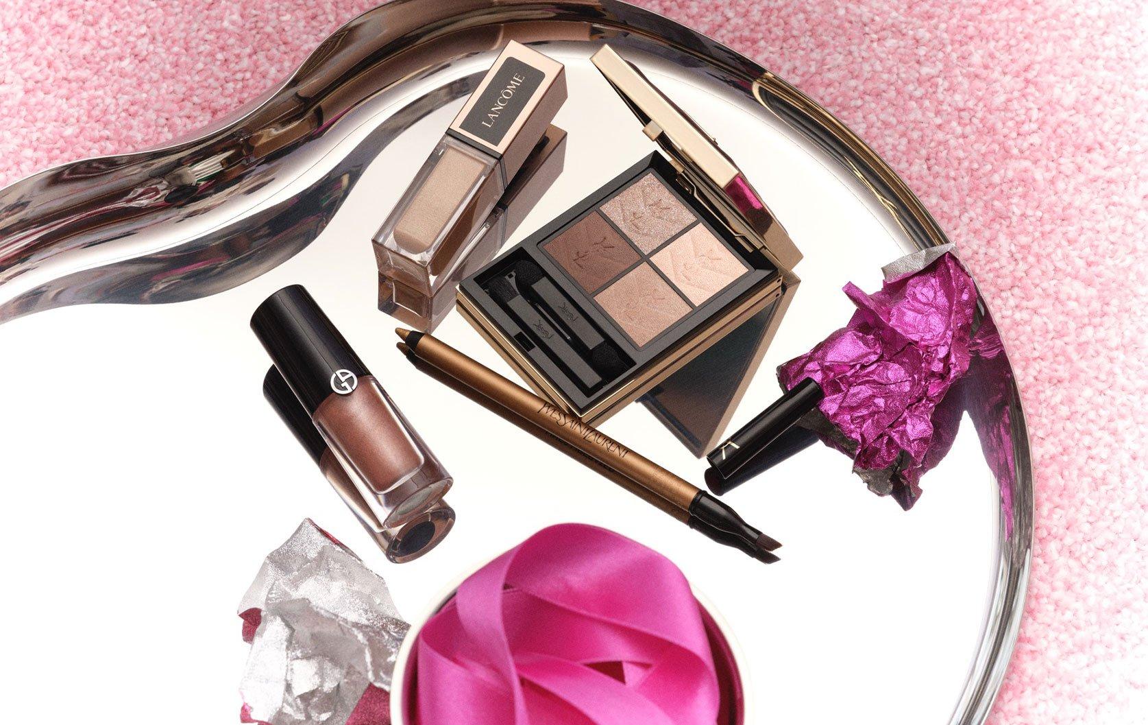 Various makeup products laid out on tray with sparkly pink background