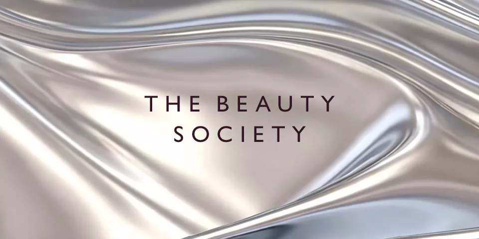The Beauty Society logo on a silver satin background
