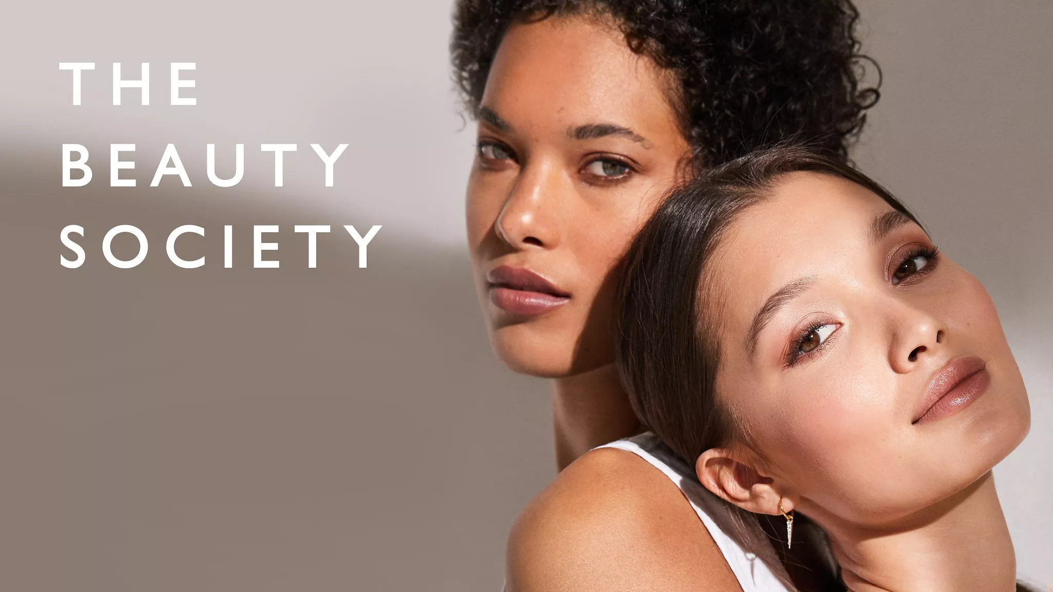 Image of two women on a earthy tone background with the words 'THE BEAUTY SOCIETY' in white on top.