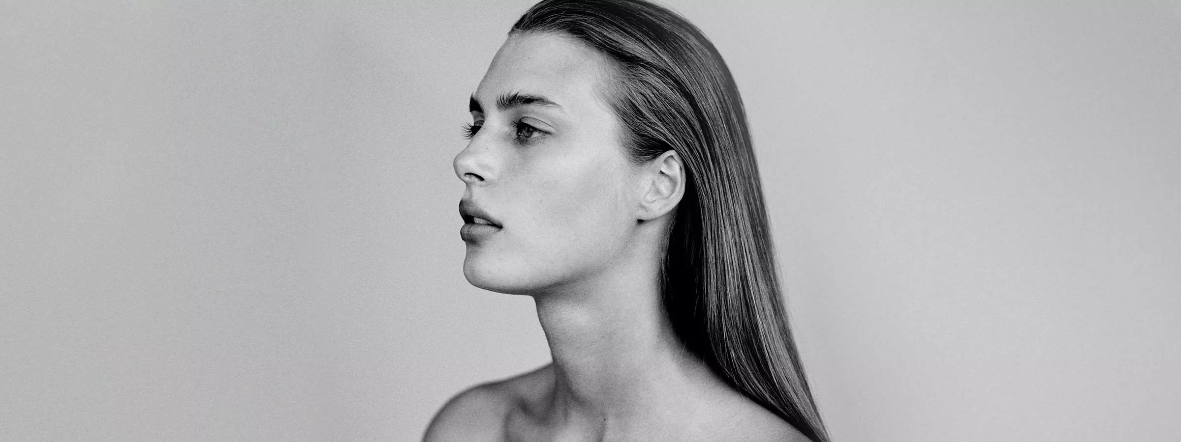 Black and white studio portrait of a woman in profile with long straight hair against a plain background