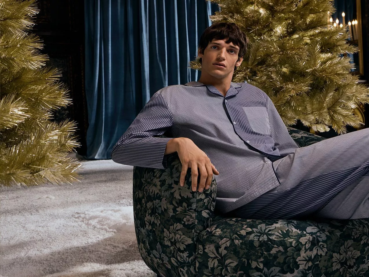 a man in stript pj's sitting on a chair with christmas trees around him