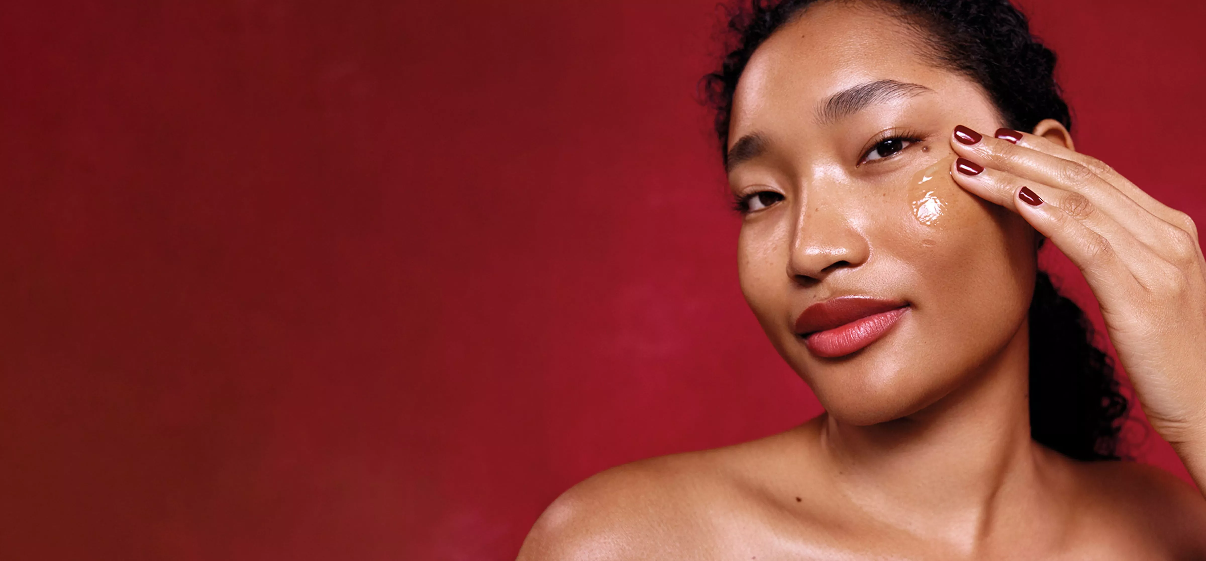 Image of a Elemis model wiping lotion on her face with a red background