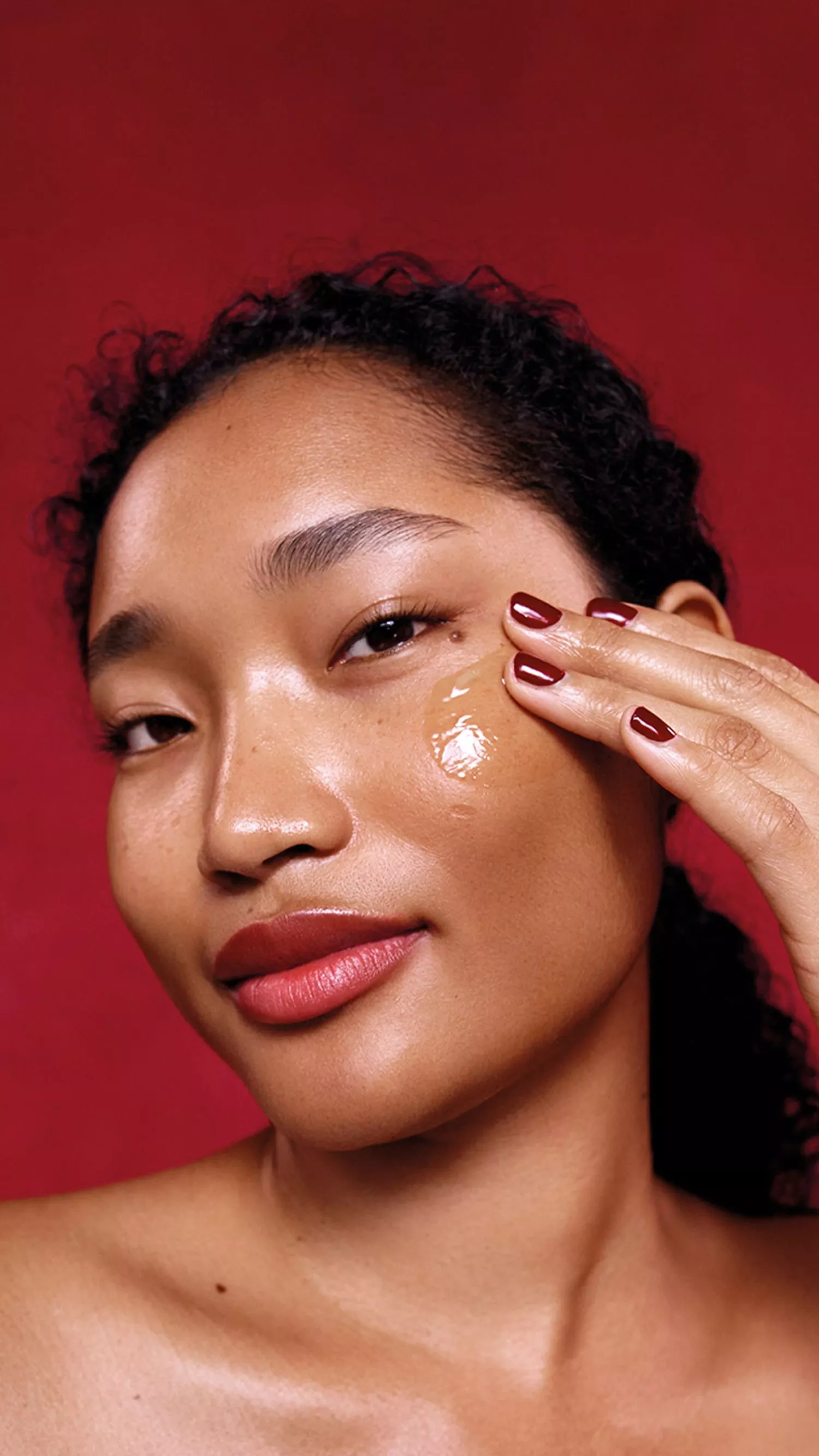 Image of a Elemis model wiping lotion on her face with a red background