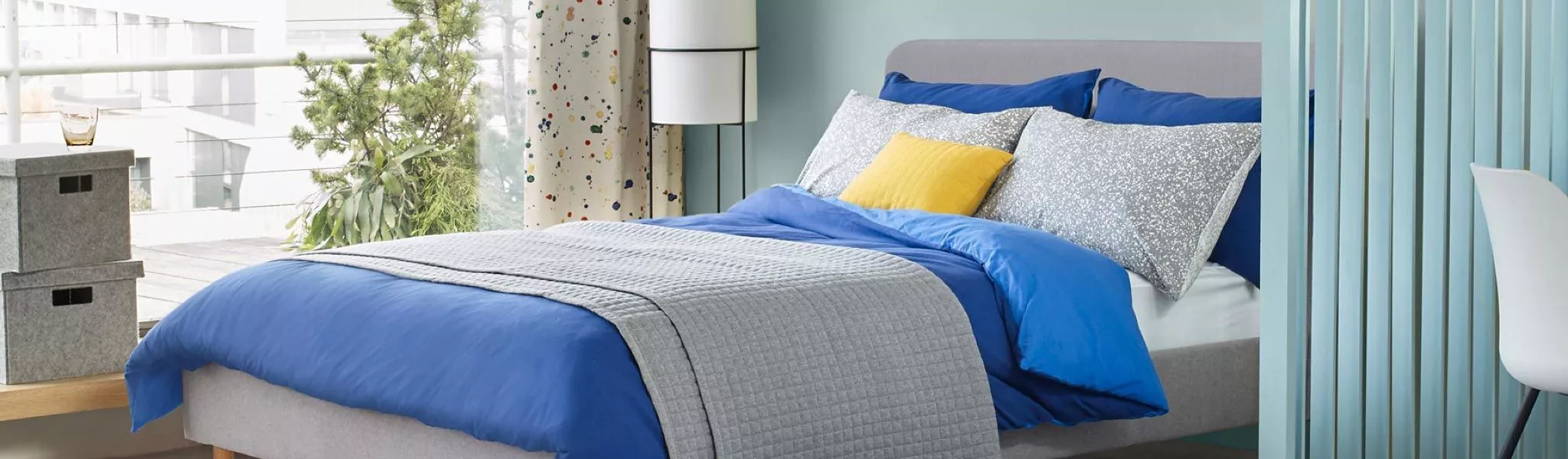 Modern bedroom with blue duvet cover set, grey quilted throw and yellow cushion on a double bed by window
