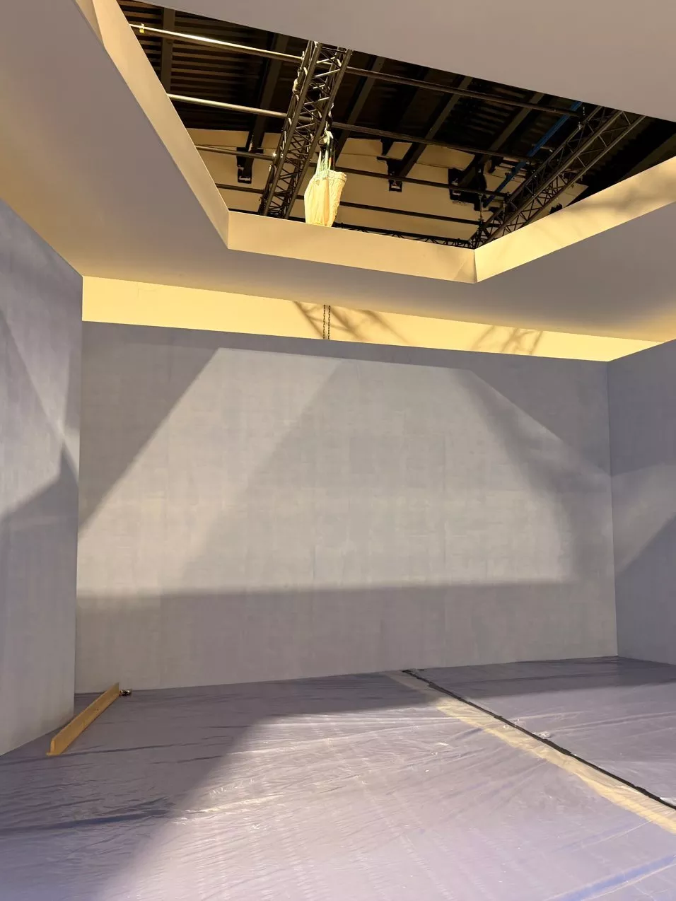 Empty exhibition stand under construction with grey walls, plastic floor covering, and overhead lighting rig.