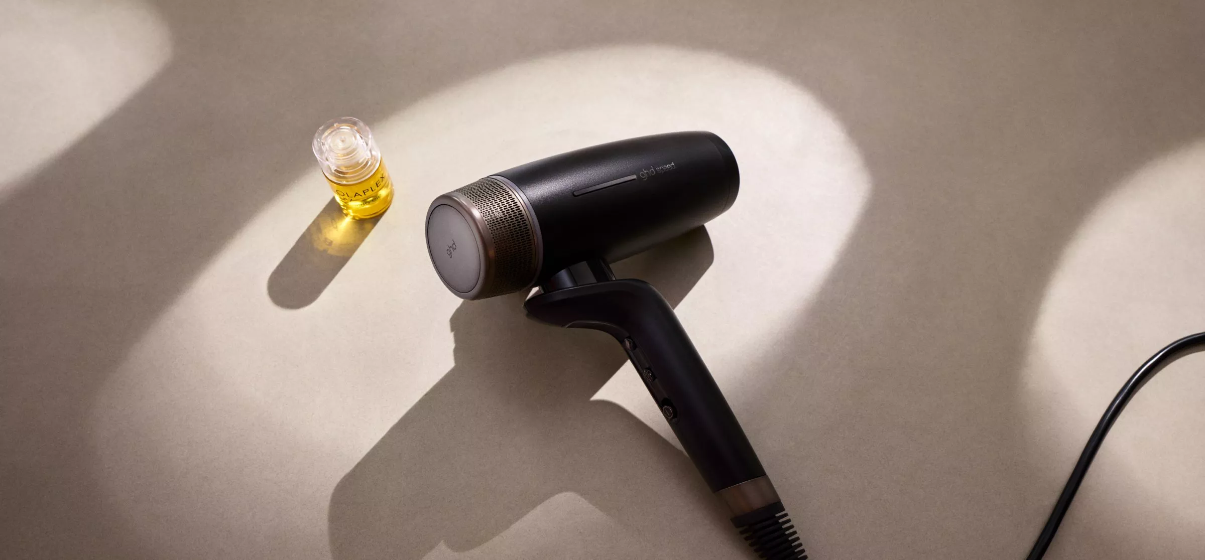 A sleek black hairdryer and a small bottle of hair oil are elegantly displayed on a neutral surface.