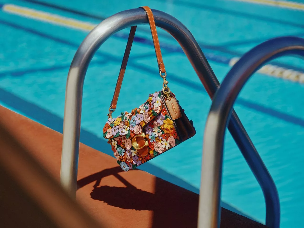 Floral leather designer handbag hanging on pool ladder by blue swimming lanes, summer fashion accessory photo