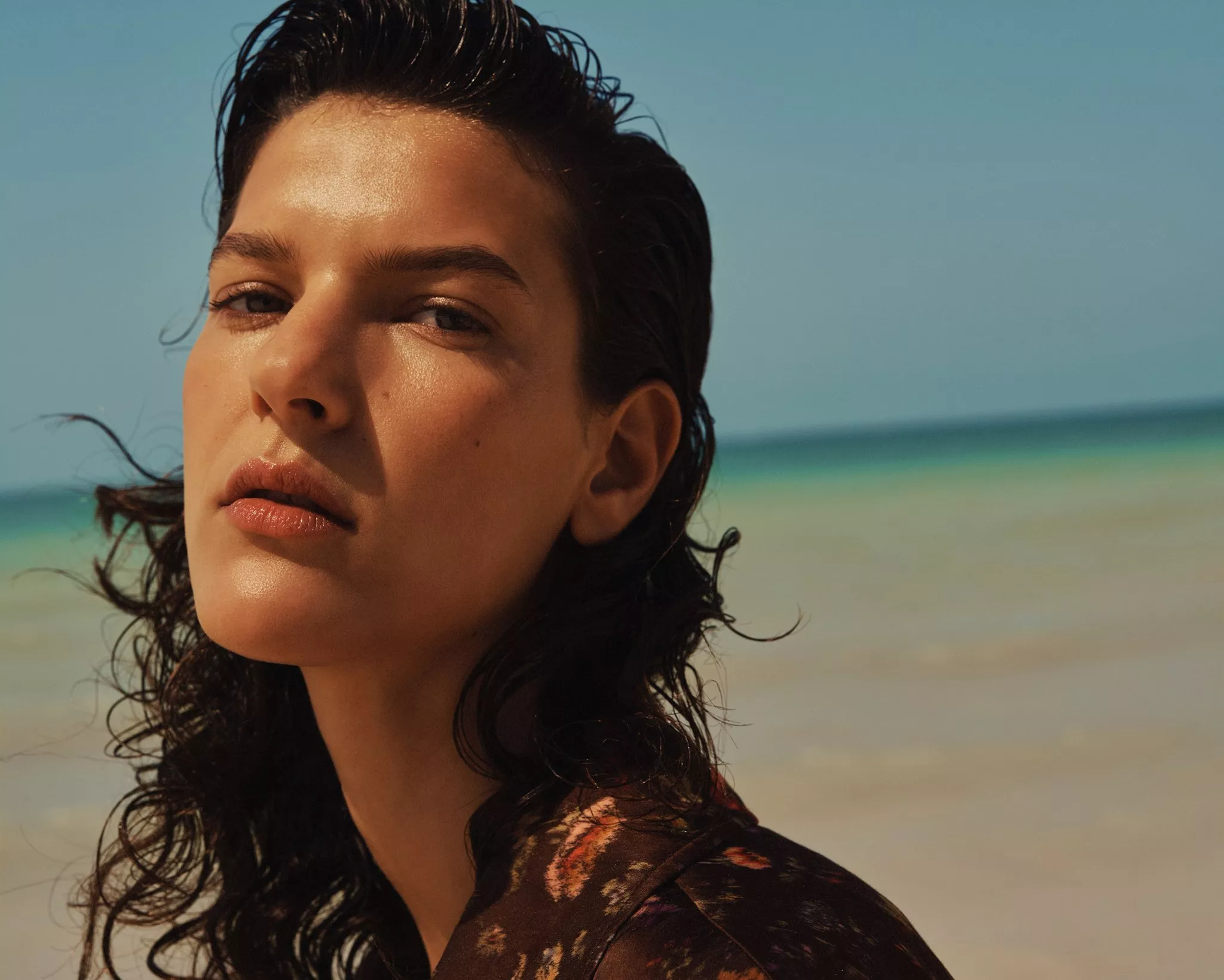 Close-up portrait of a woman by the sea, natural makeup and wet-look hair, summer beach beauty photography.