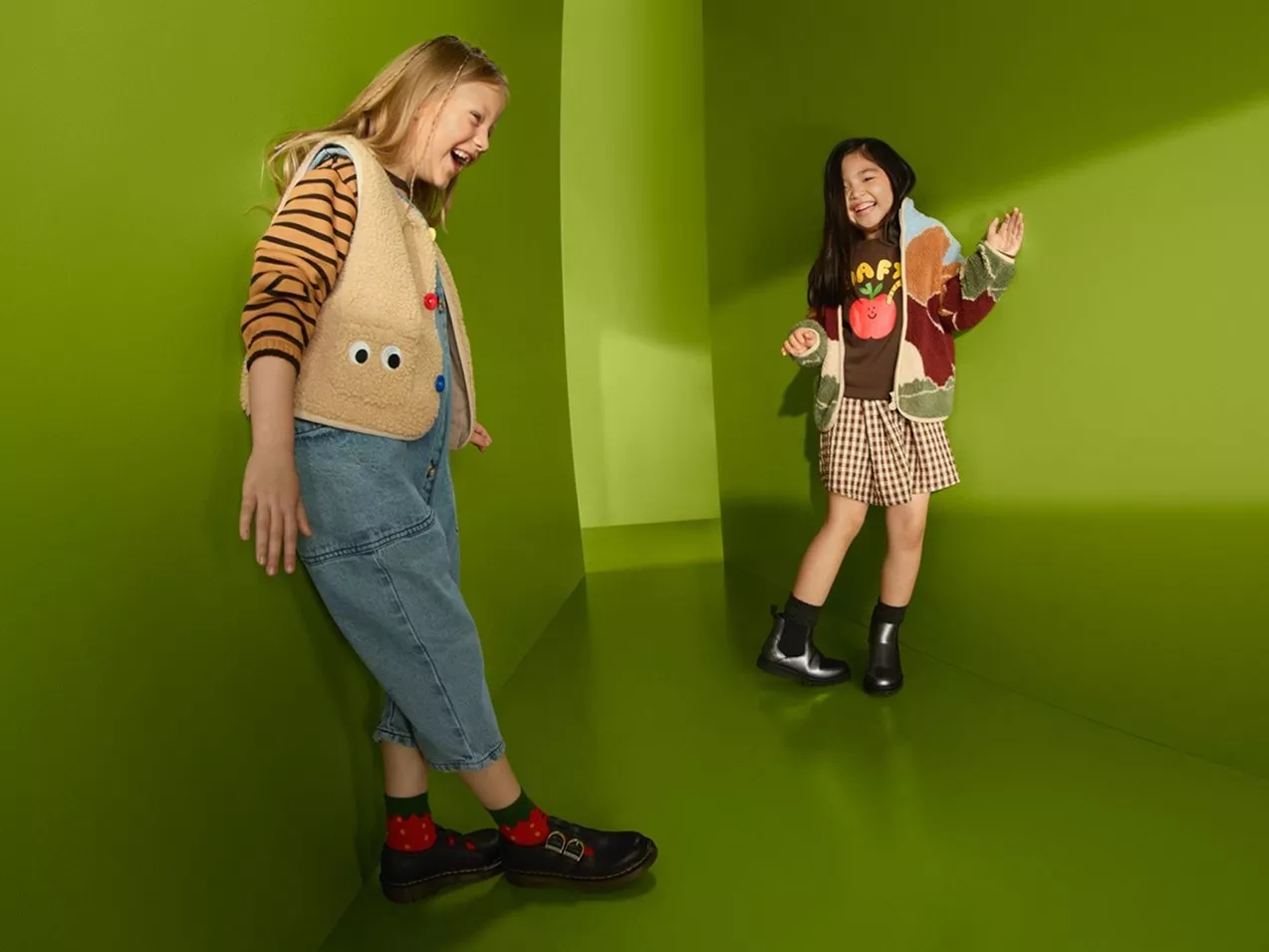 Two children in colourful autumn outfits and boots laughing in a bright green studio