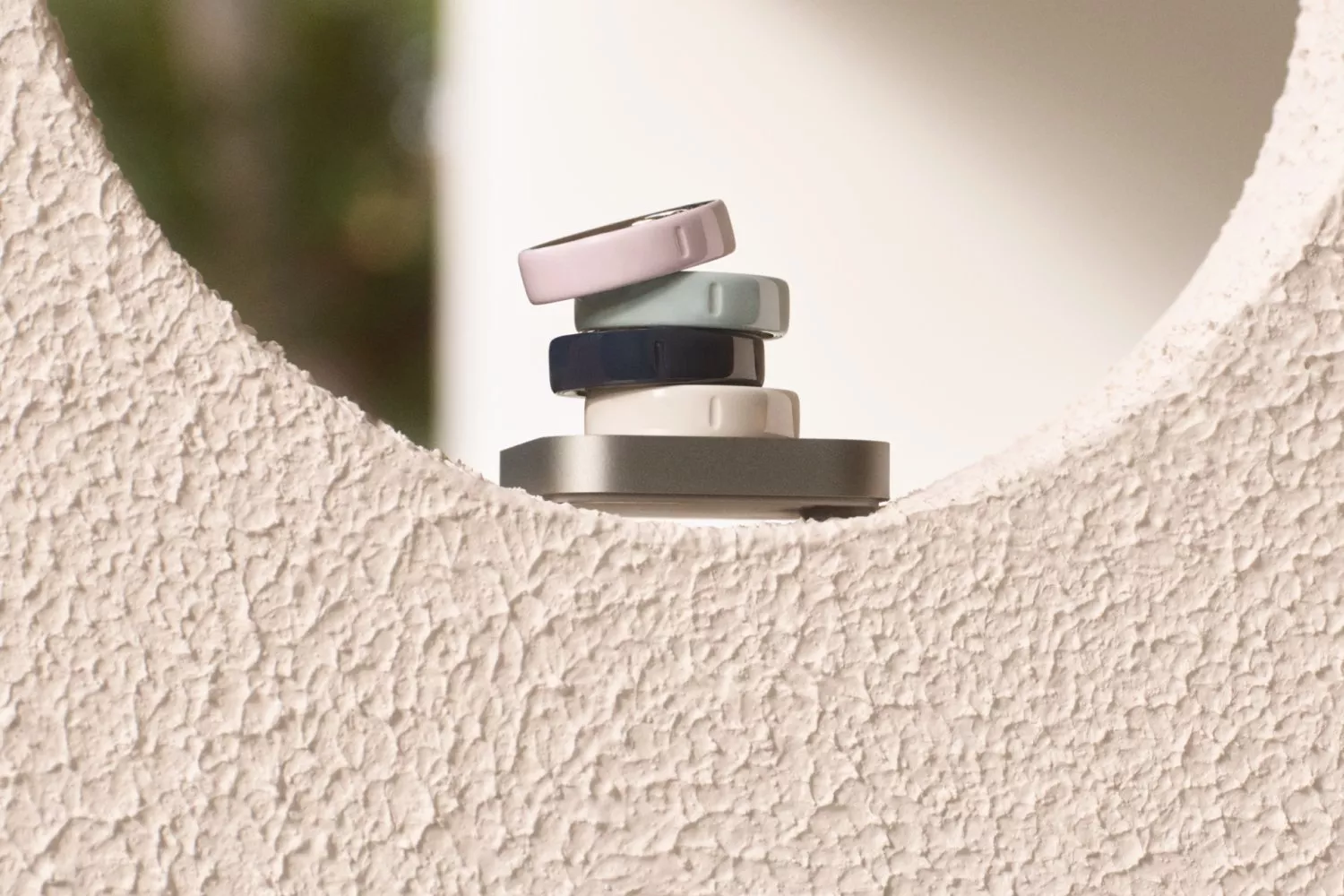 Stacked silicone smart rings in pastel colours on a pedestal, framed by a textured plaster archway background