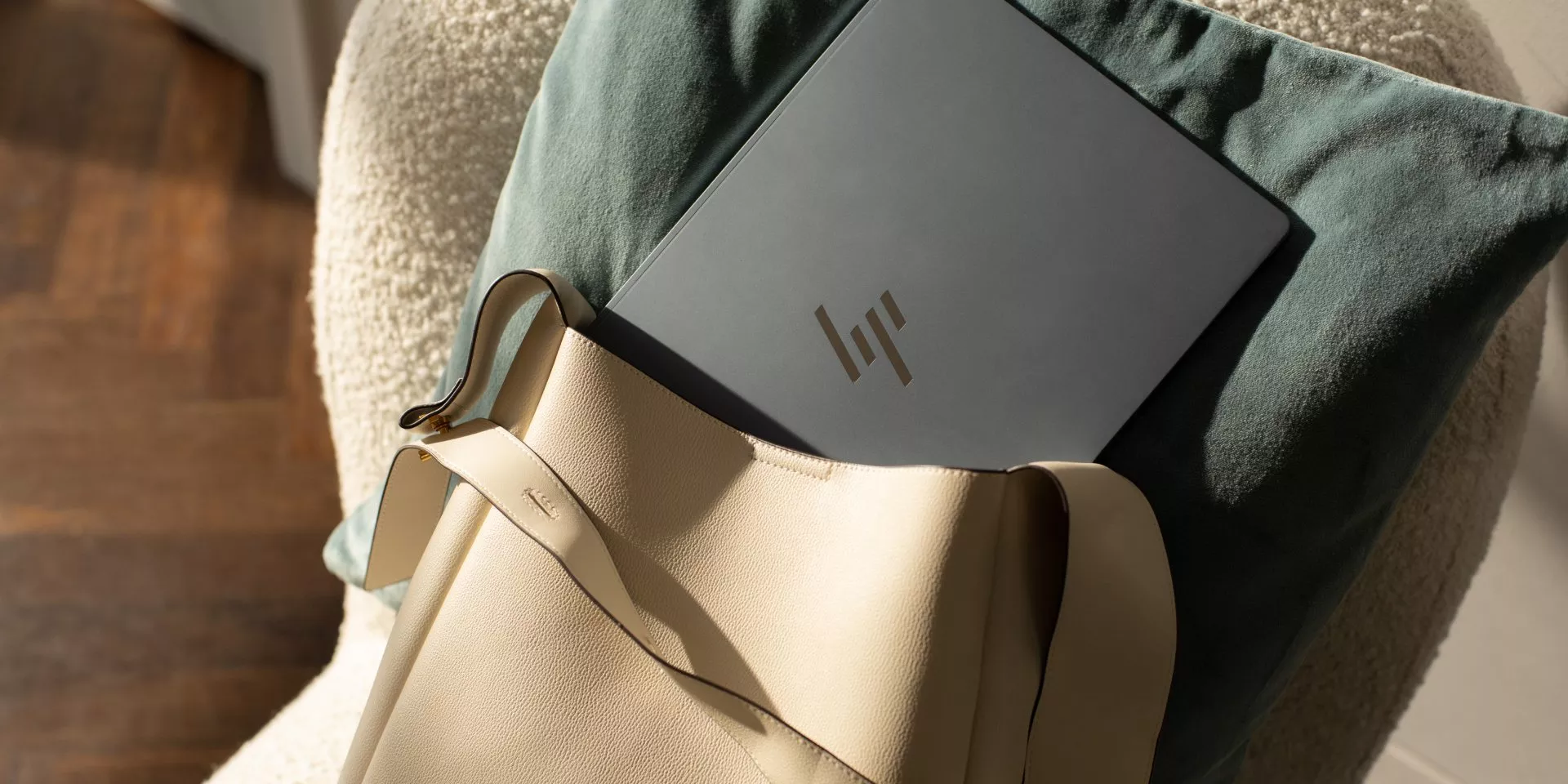 Silver laptop in beige leather tote bag on armchair with green cushion, modern work from home setup in sunlight