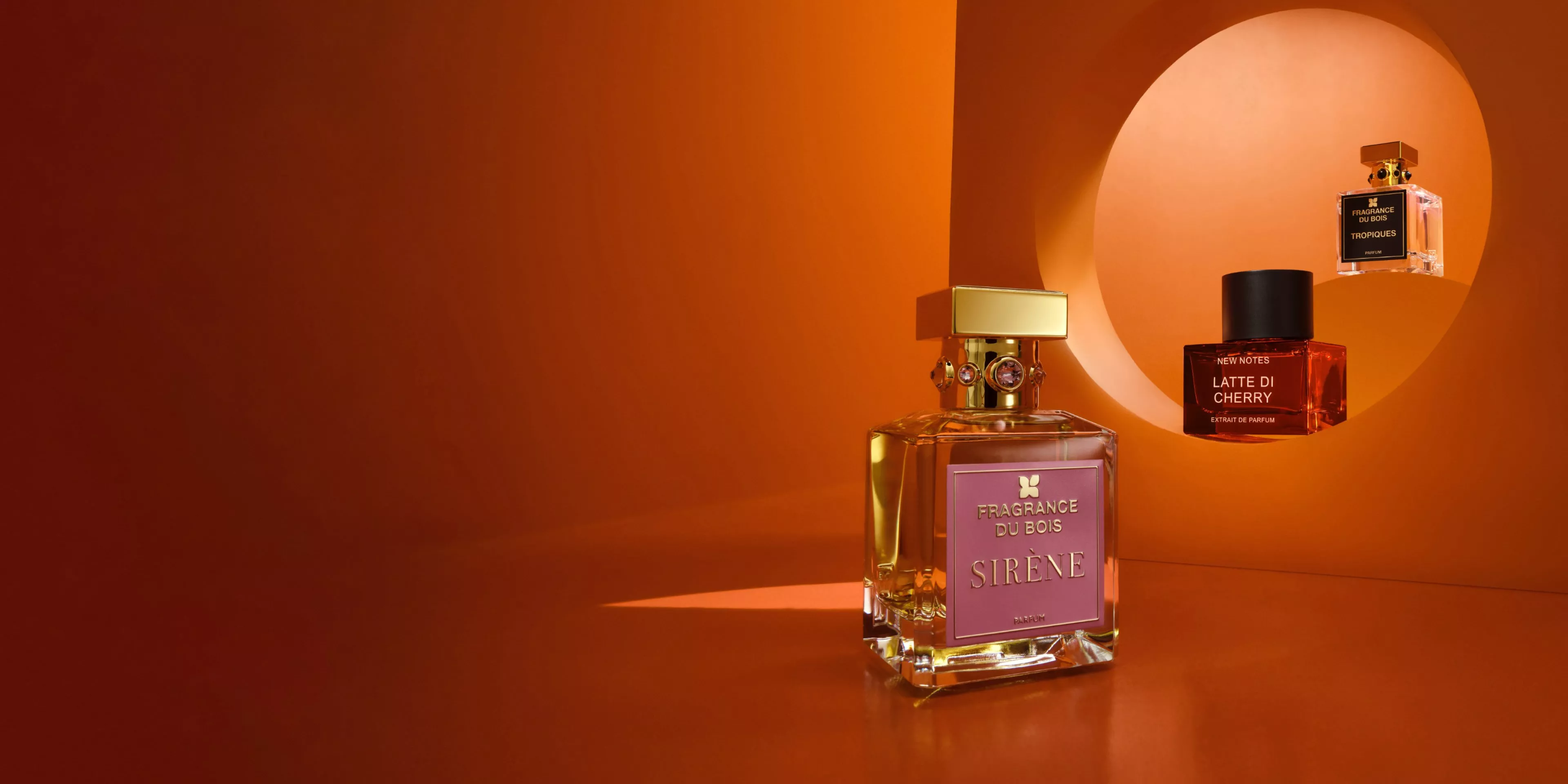 Luxury perfume bottles on warm orange backdrop, featuring Fragrance du Bois Sirène and New Notes Latte di Cherry