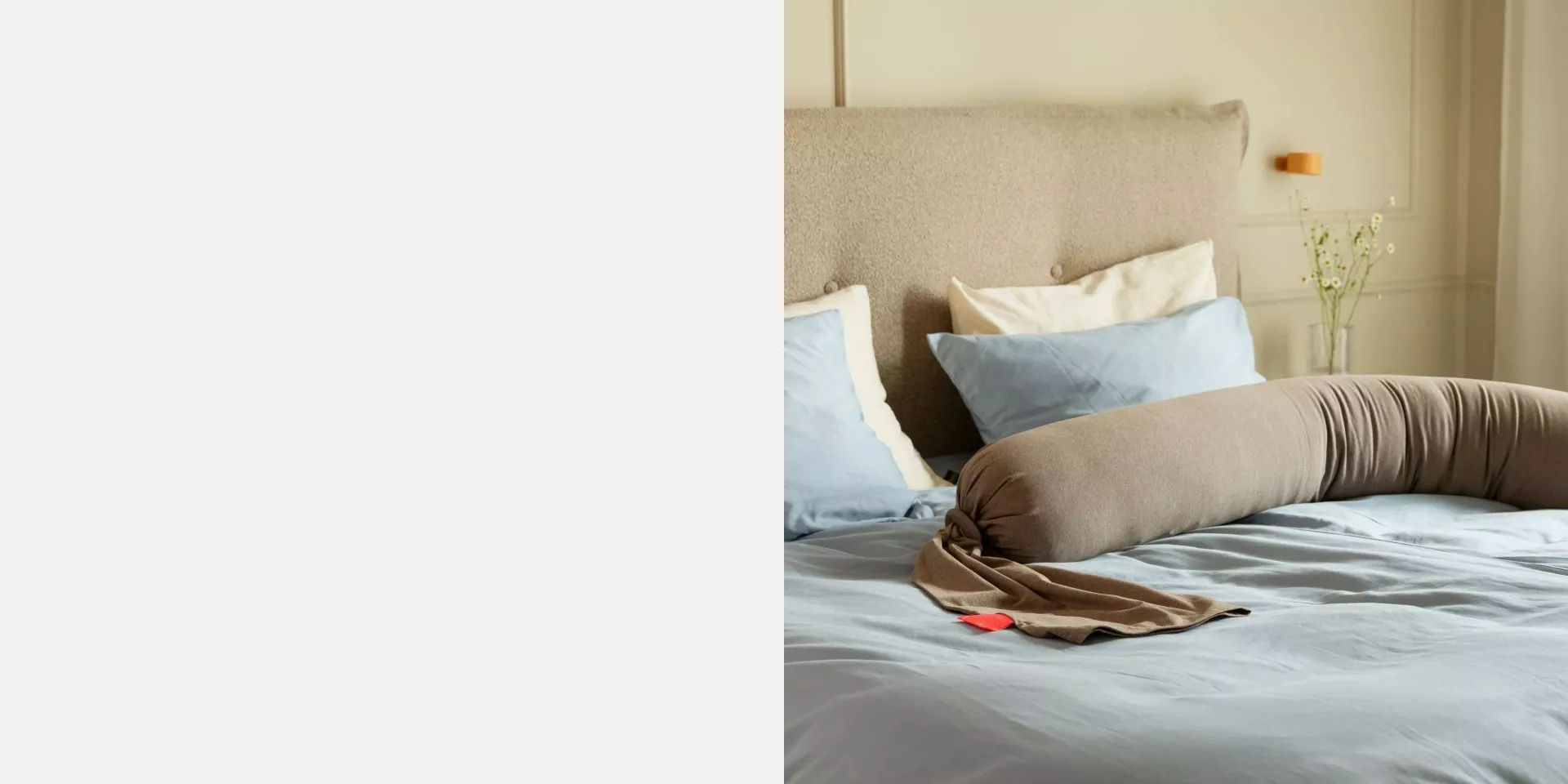 Modern bedroom with upholstered headboard, blue bedding and pregnancy pillow in soft natural light